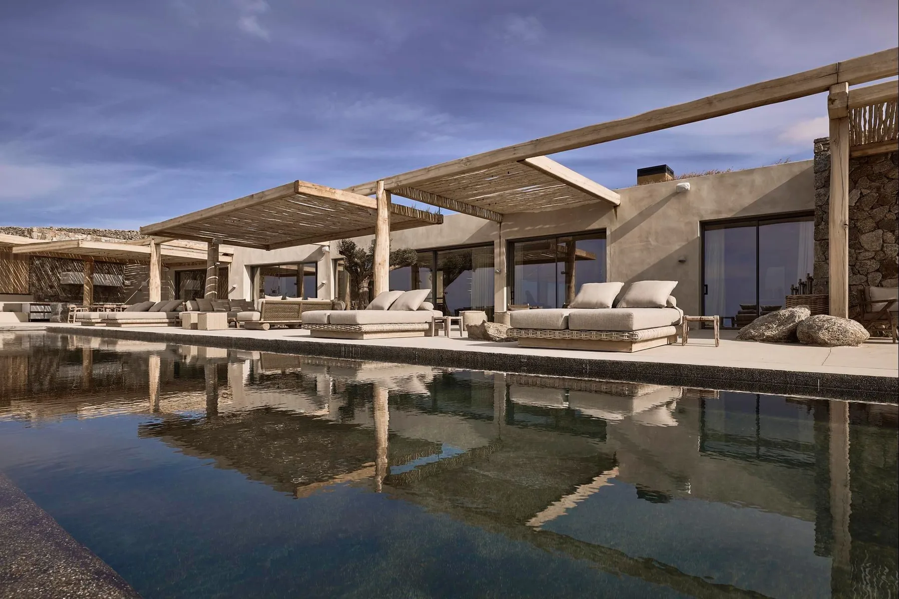 An outdoor pool in front of a modern building with shaded seating areas.