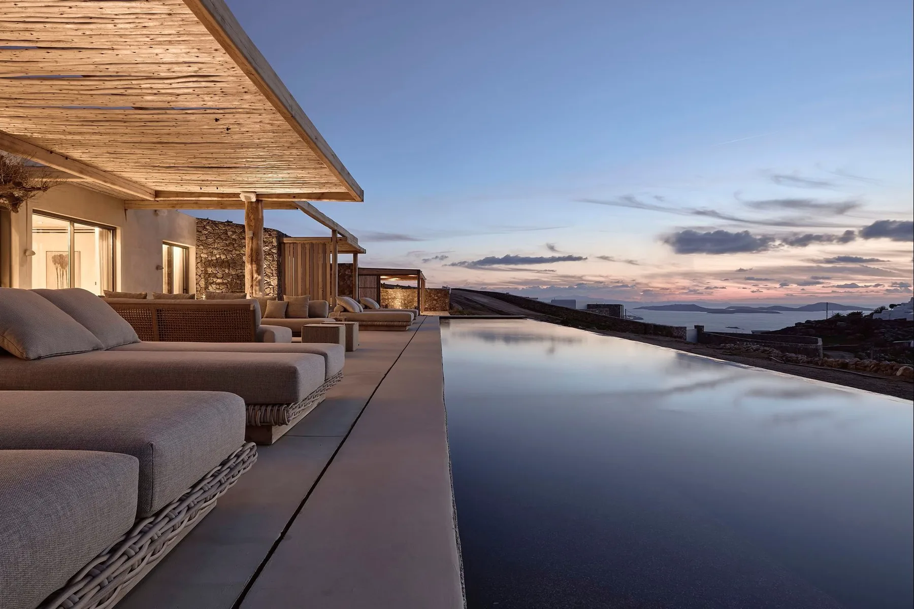 An outdoor seating area beside an infinity pool at dusk.