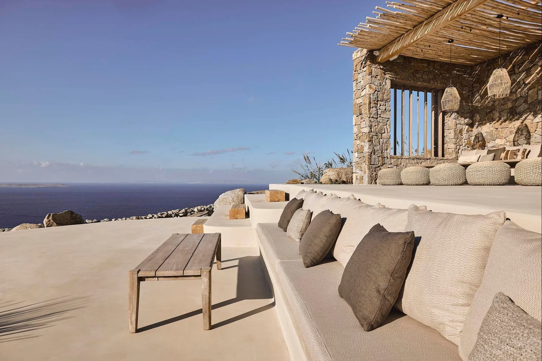 An outdoor lounge terrace overlooks the sea, with built-in seating and a shaded stone pavilion.