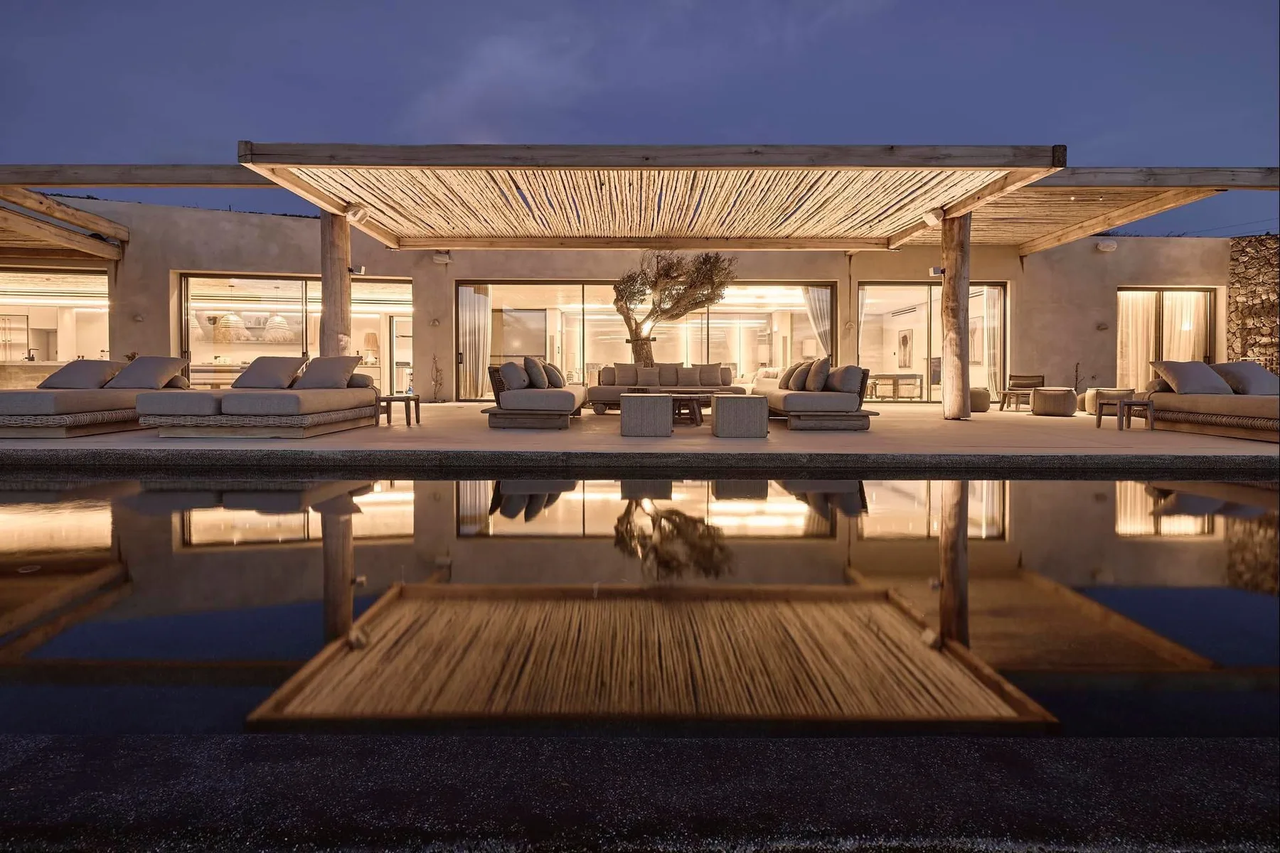 Outdoor lounge beside a reflecting pool, shaded by a woven pergola.
