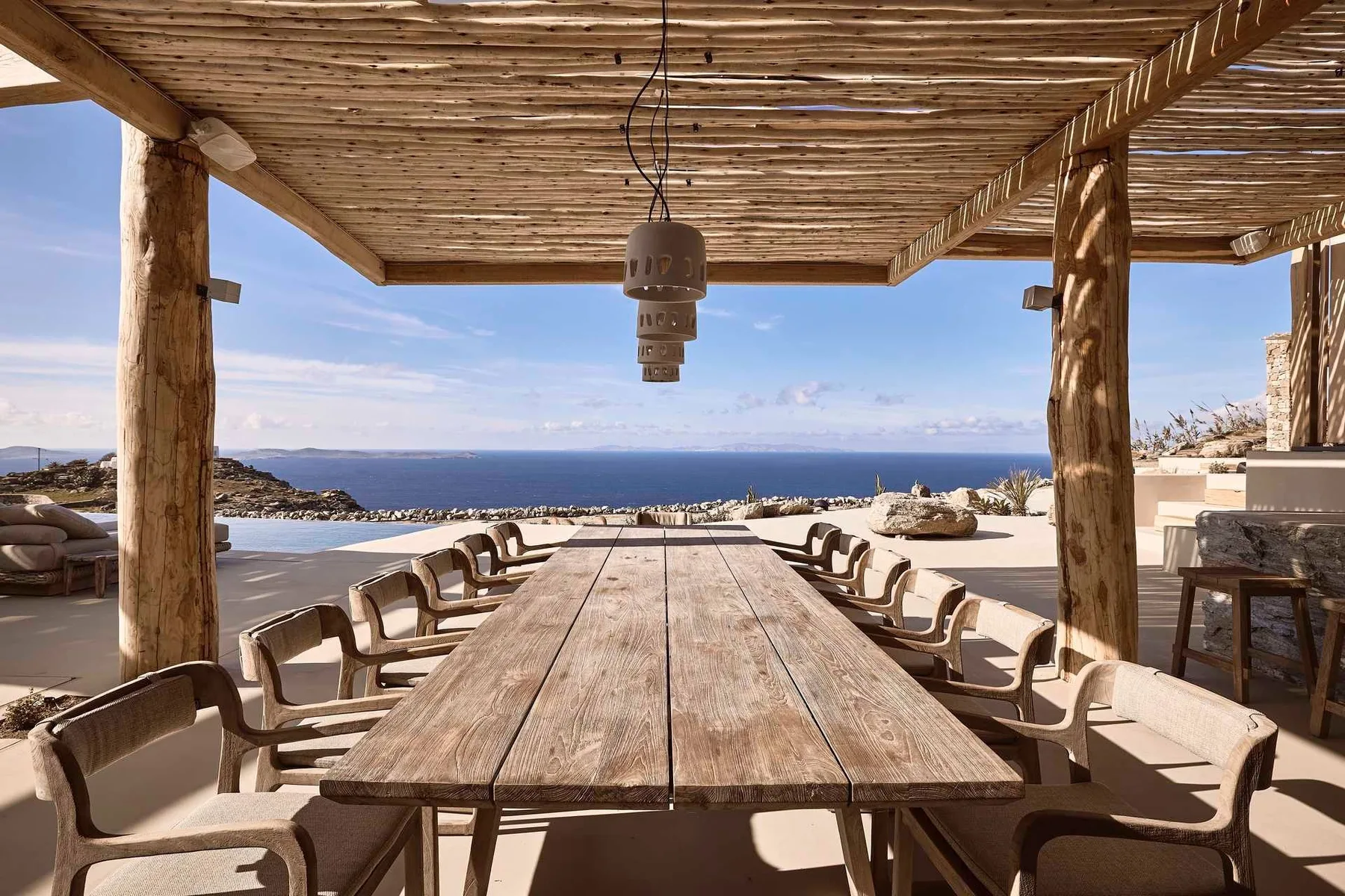 An outdoor dining area with a long table and chairs overlooks the sea.