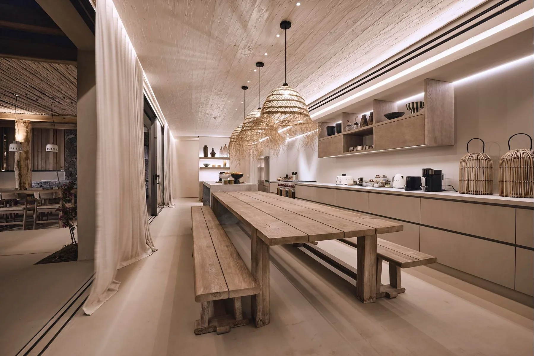 A spacious kitchen and dining area with a long wooden table and hanging lights.