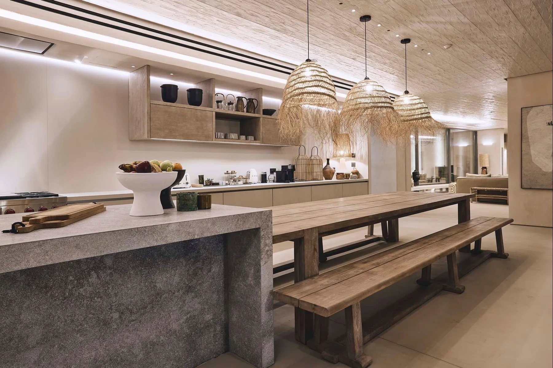 A modern kitchen and dining area with a long wooden table beneath woven pendant lights.