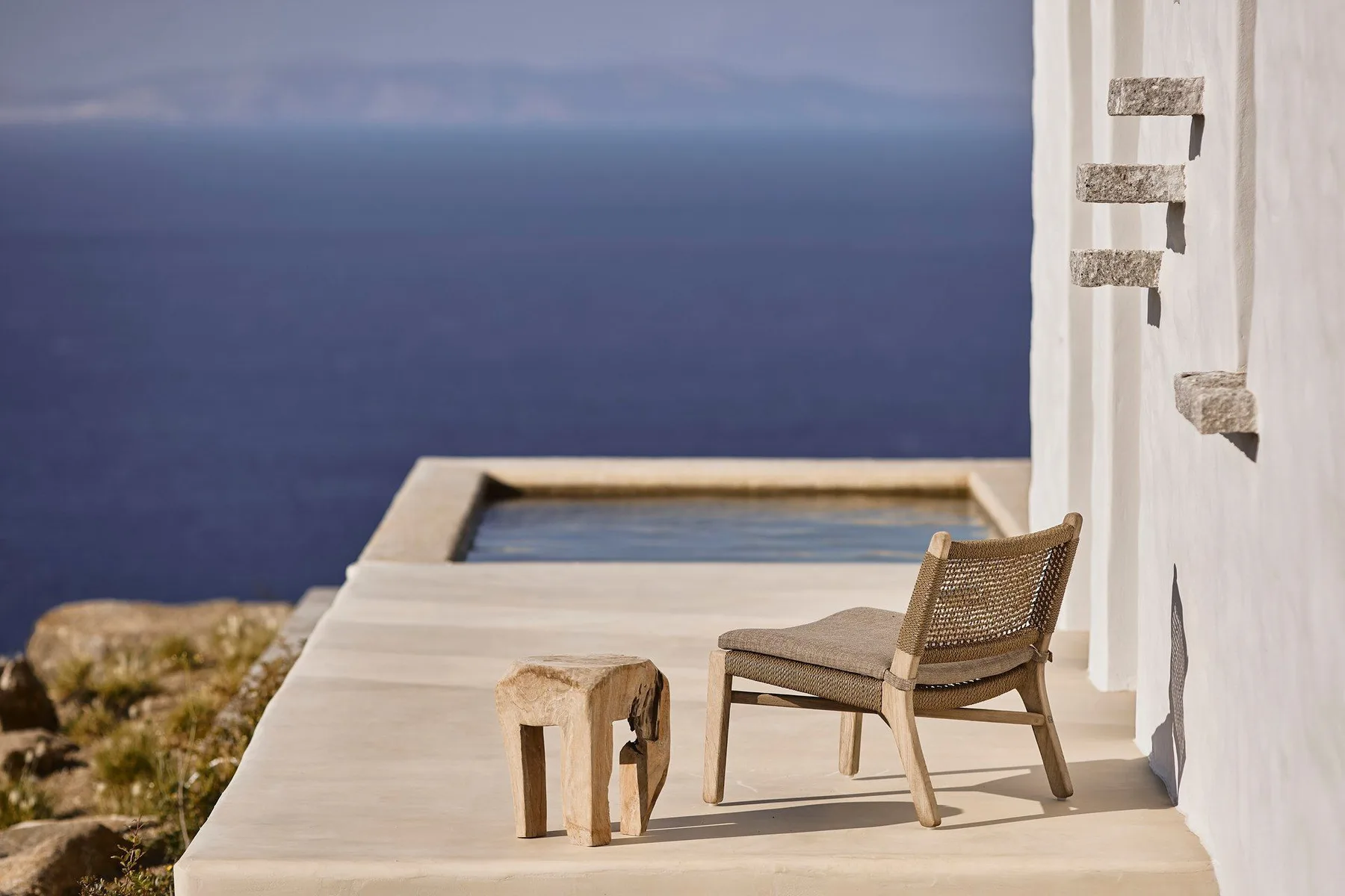 A chair and small table sit on a terrace overlooking the sea.