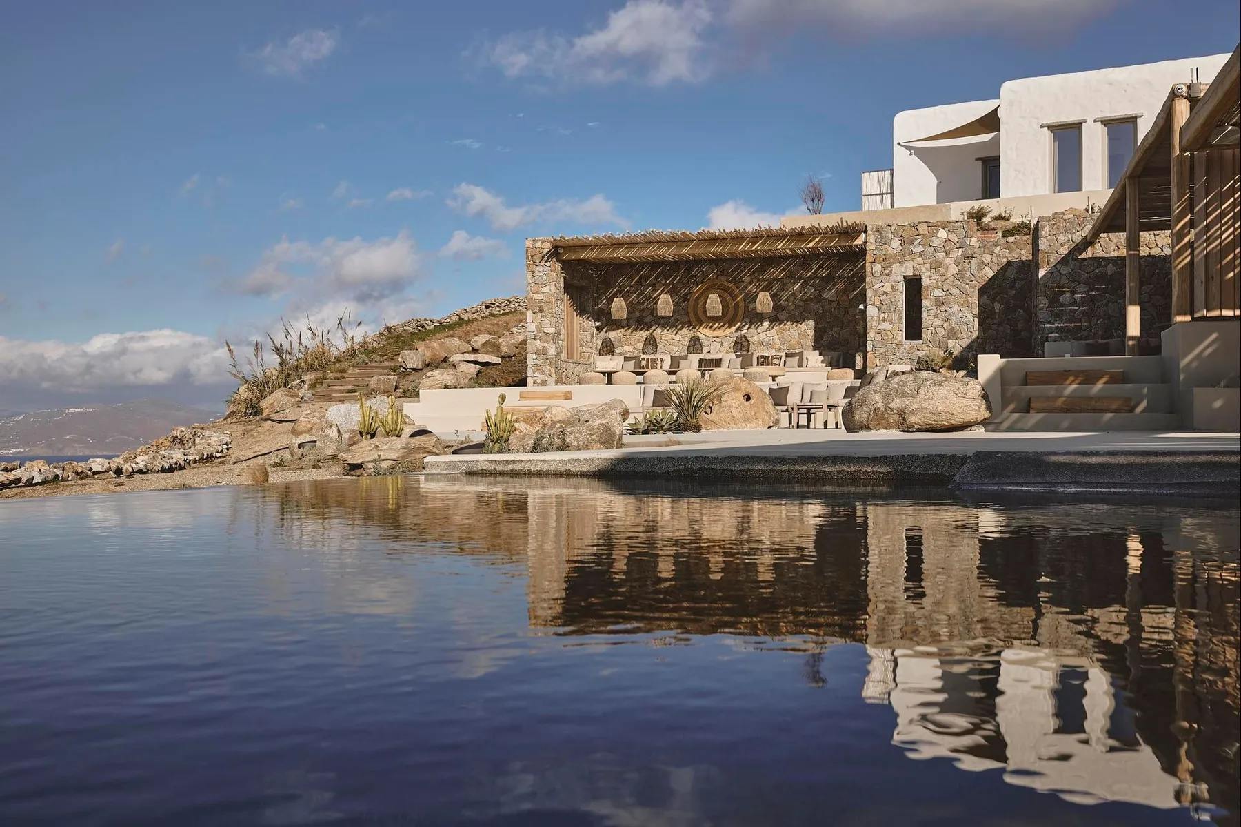 A stone poolside terrace with seating overlooks a calm pool and distant hills.