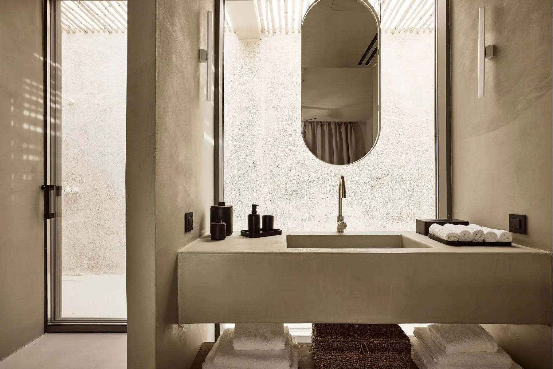 A bathroom vanity with a sink and oval mirror beside a glass shower.
