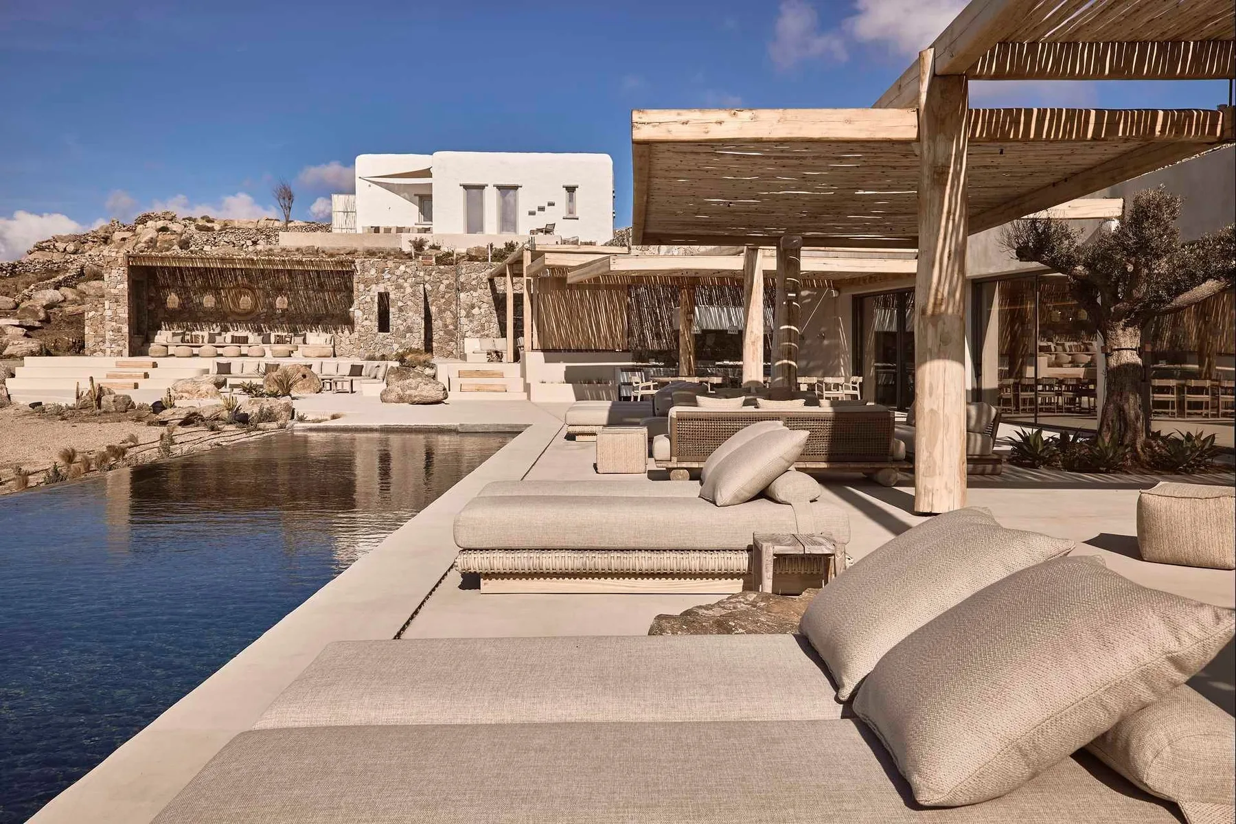 Outdoor poolside lounge with cushioned seating beneath a wooden pergola.