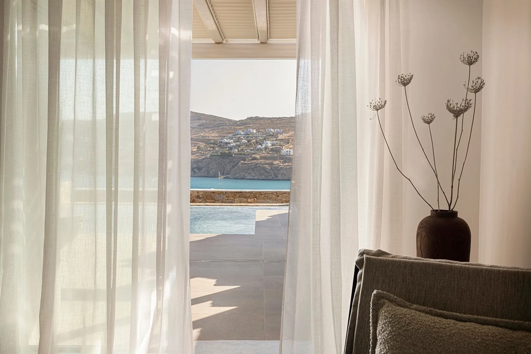 A bright interior opens through sheer curtains to a terrace and sea view.
