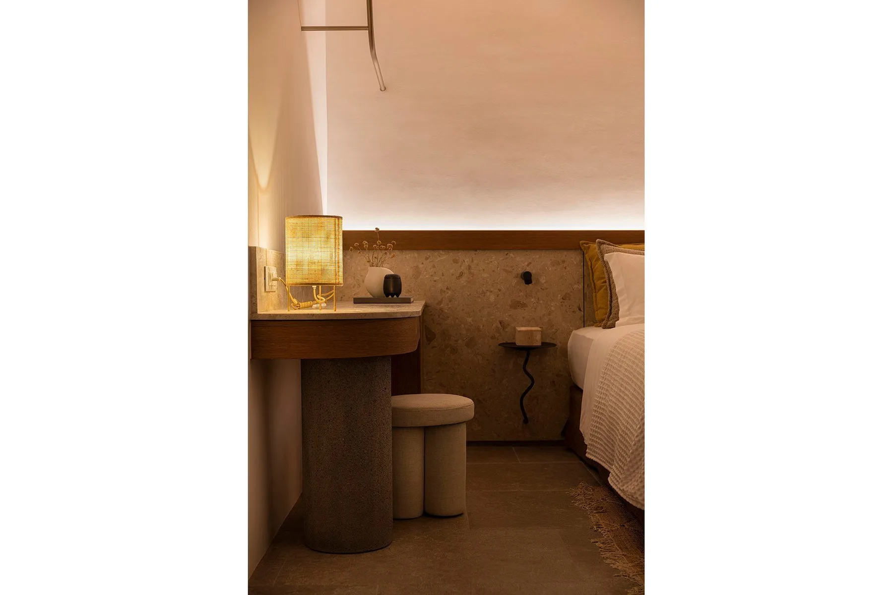 A bedroom with a bedside table and a lit lamp beside the bed.