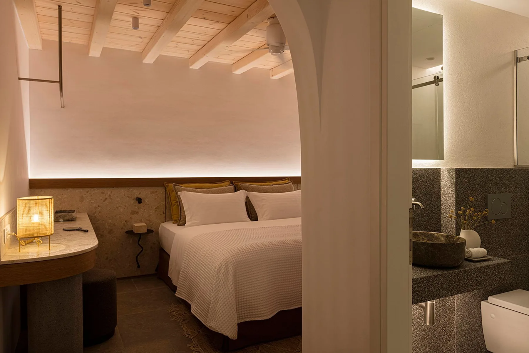 A bedroom with a neatly made bed beside an open bathroom vanity.