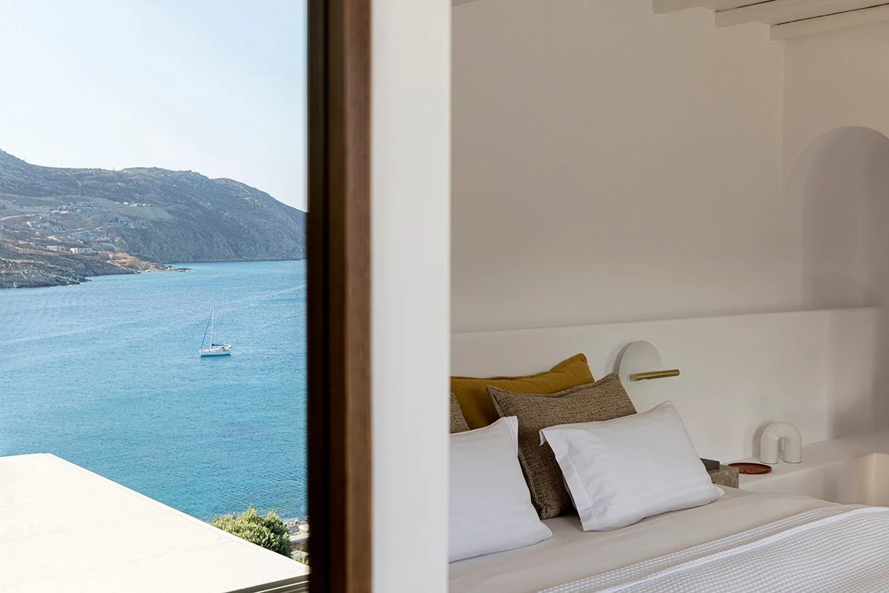 A bedroom with a bed beside a large window overlooking the water.
