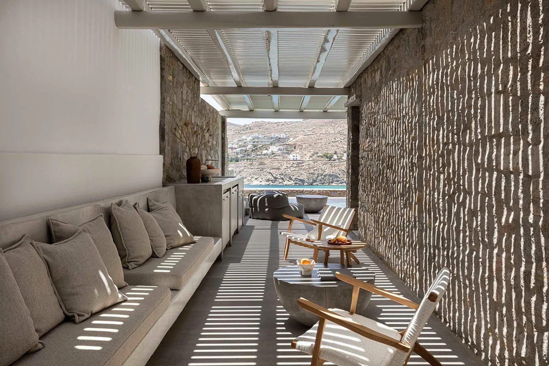 A covered outdoor lounge with cushioned seating and a view of the water.