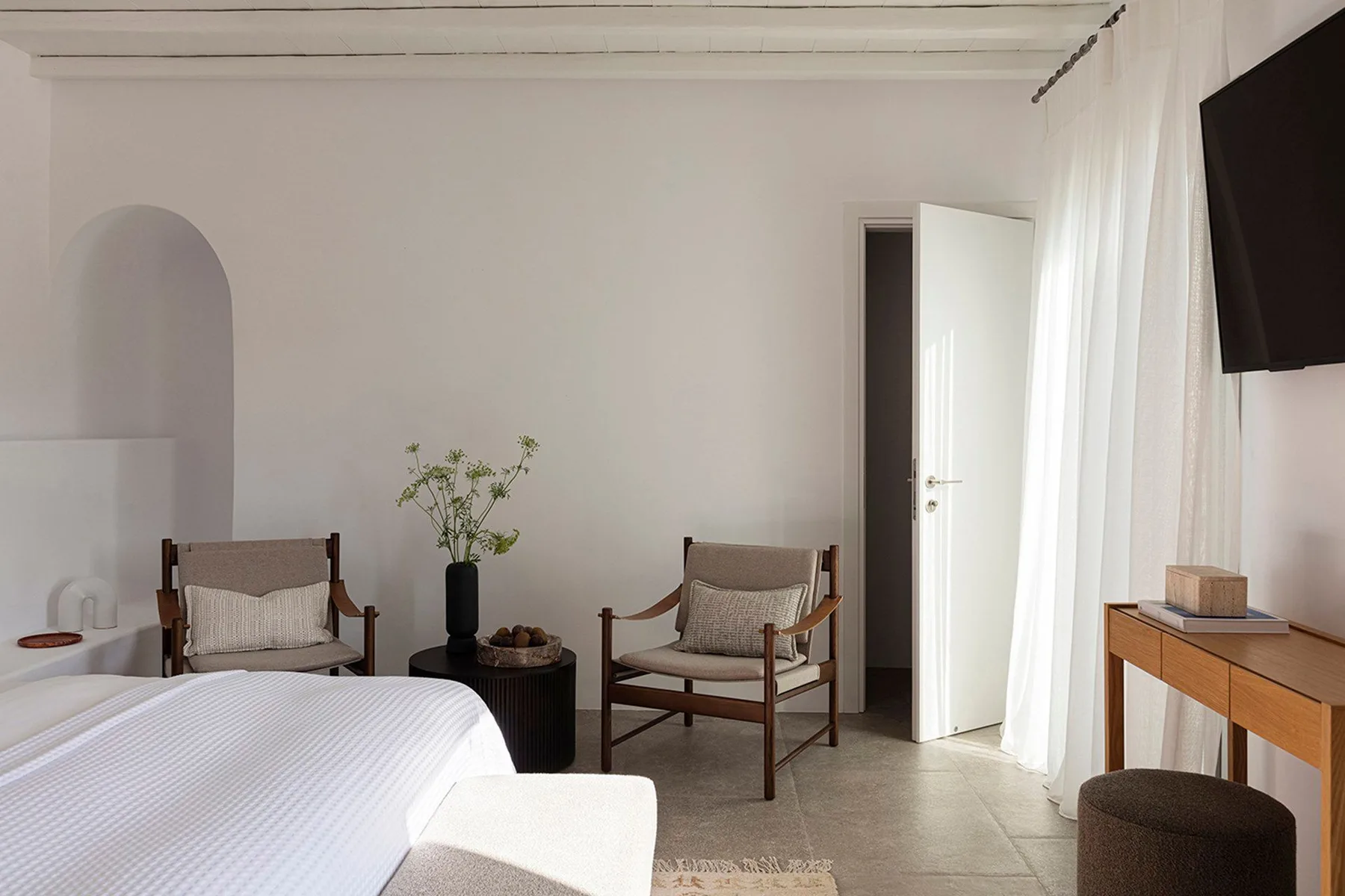 A bright bedroom with a bed, two chairs, and an open door.