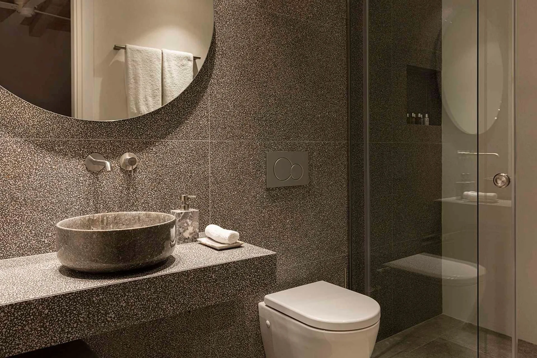 A modern bathroom with a stone sink, toilet, and glass shower.