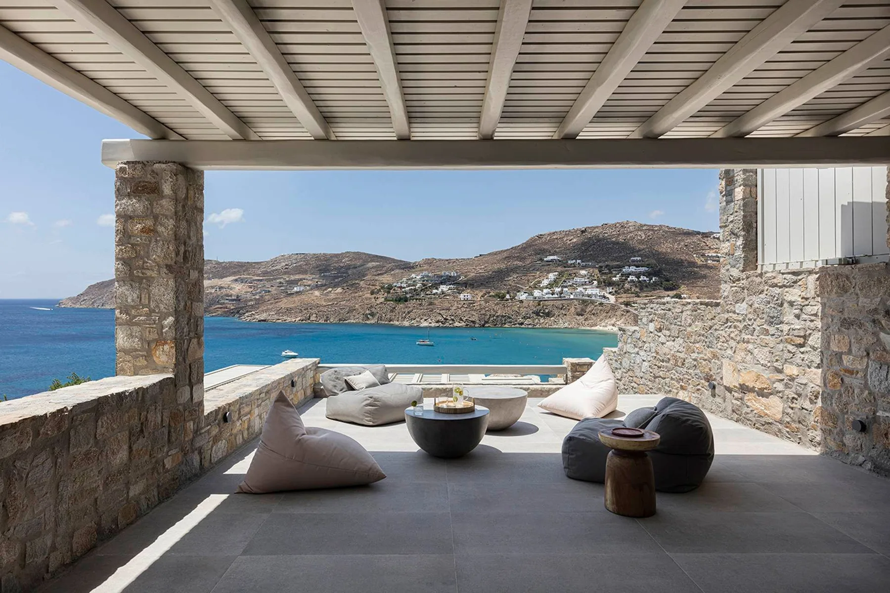 A covered seaside terrace with cushioned seating and views across the water.