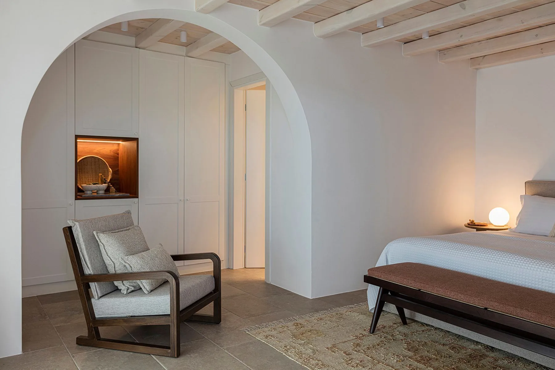 A bedroom with a bed, a cushioned chair, and an arched doorway.