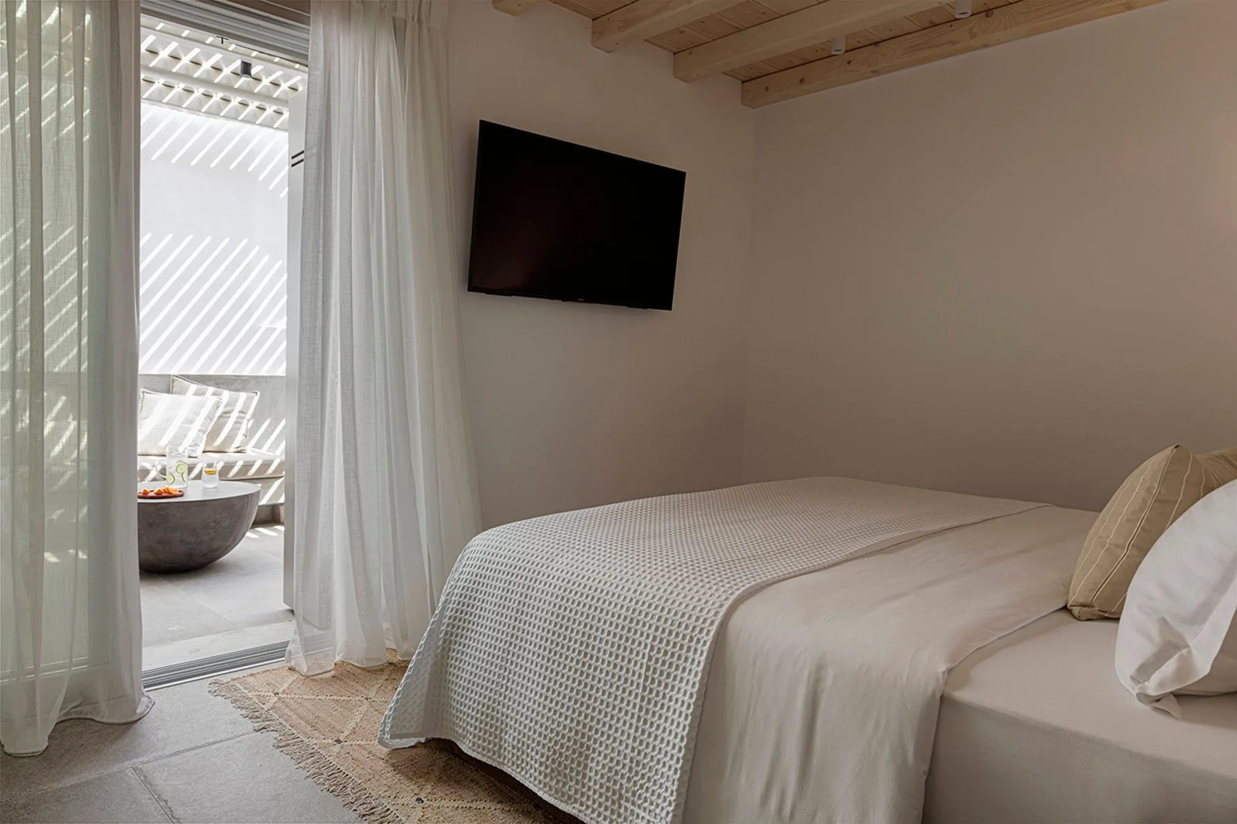 A bedroom with a neatly made bed and a television mounted on the wall.