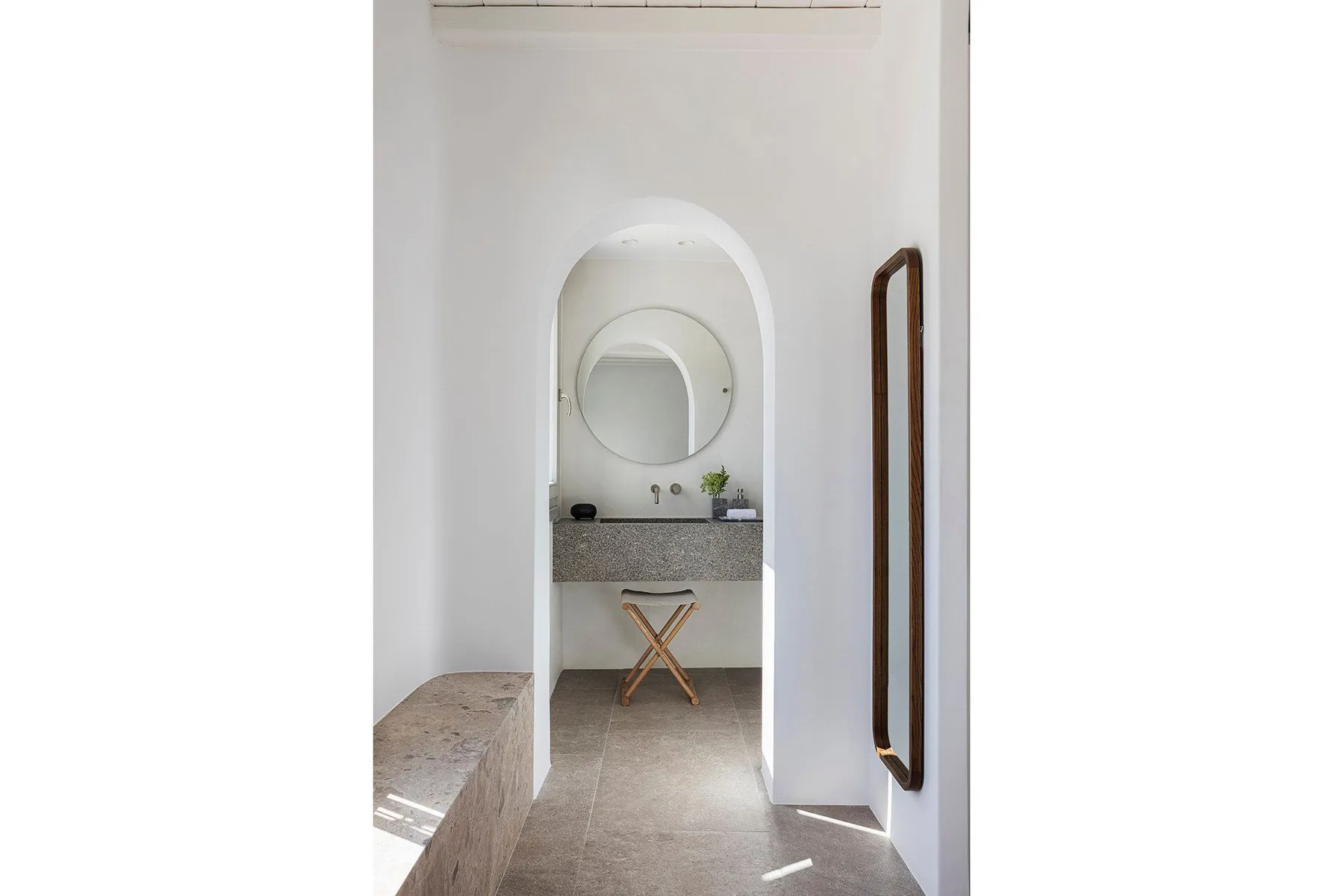 A bathroom vanity sits beyond an arched opening, with a round mirror above the sink.