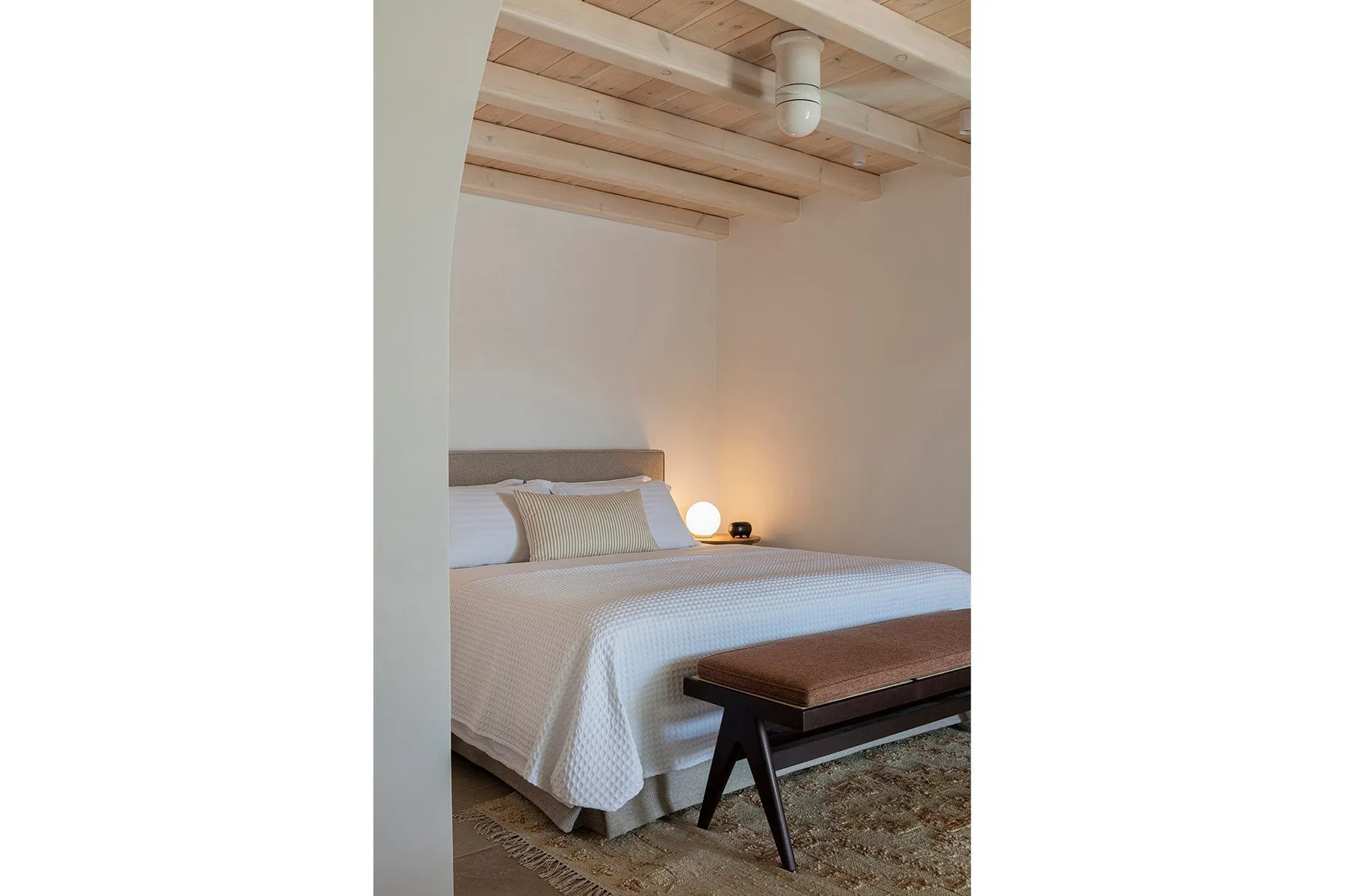 A bedroom with a neatly made bed and a wooden bench at its foot.