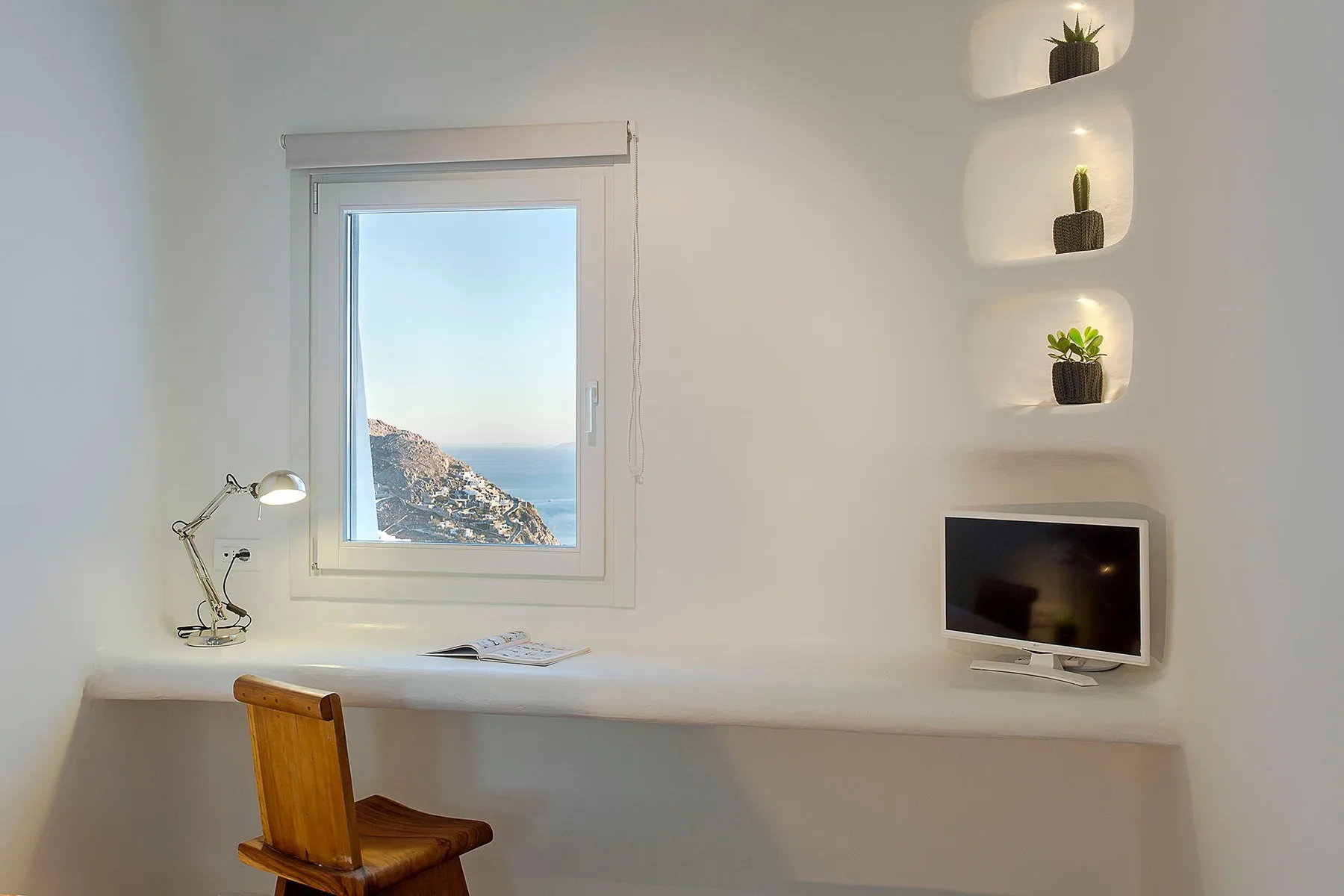 A bright workspace with a desk, chair, and window overlooking the sea.