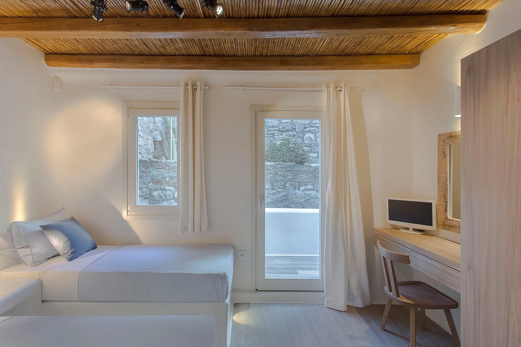 A bright bedroom with a bed, tall windows, and a desk by the wall.