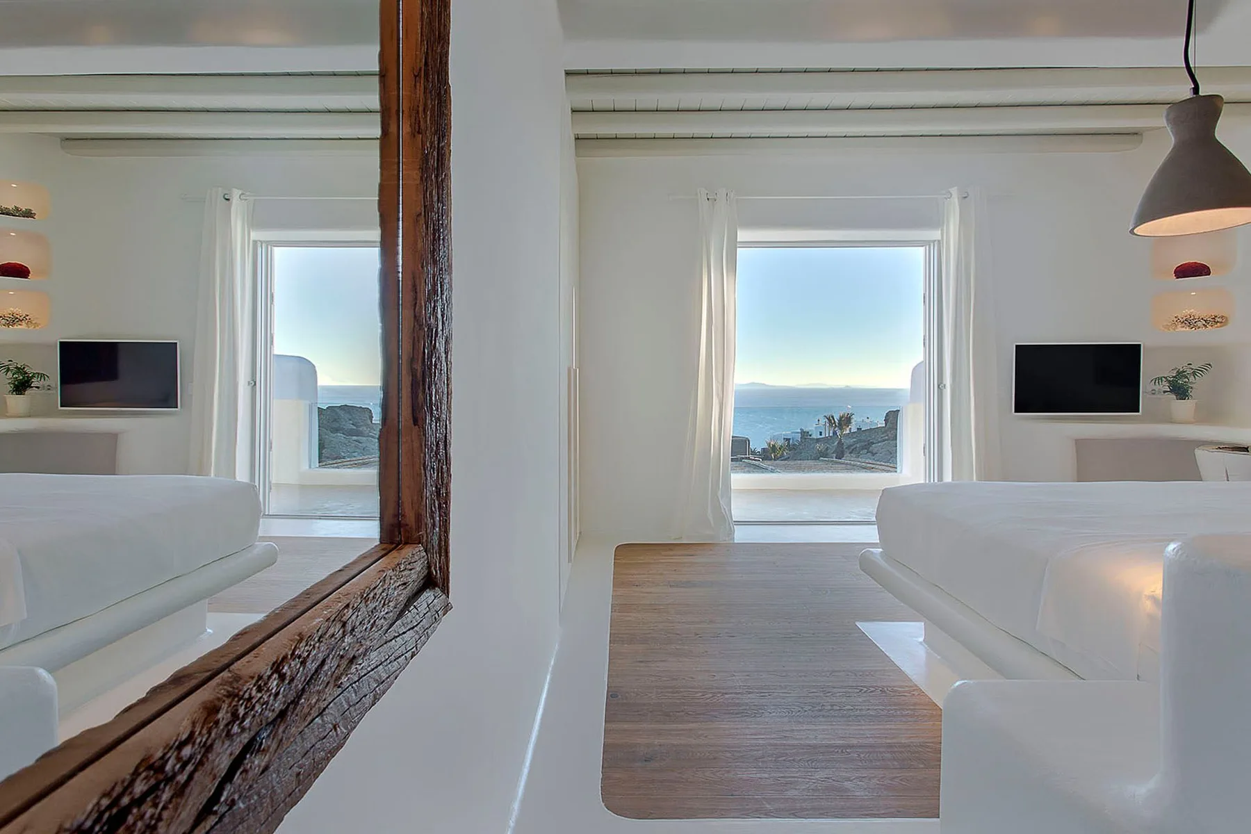 A bright living room with white seating and a large window overlooking the sea.