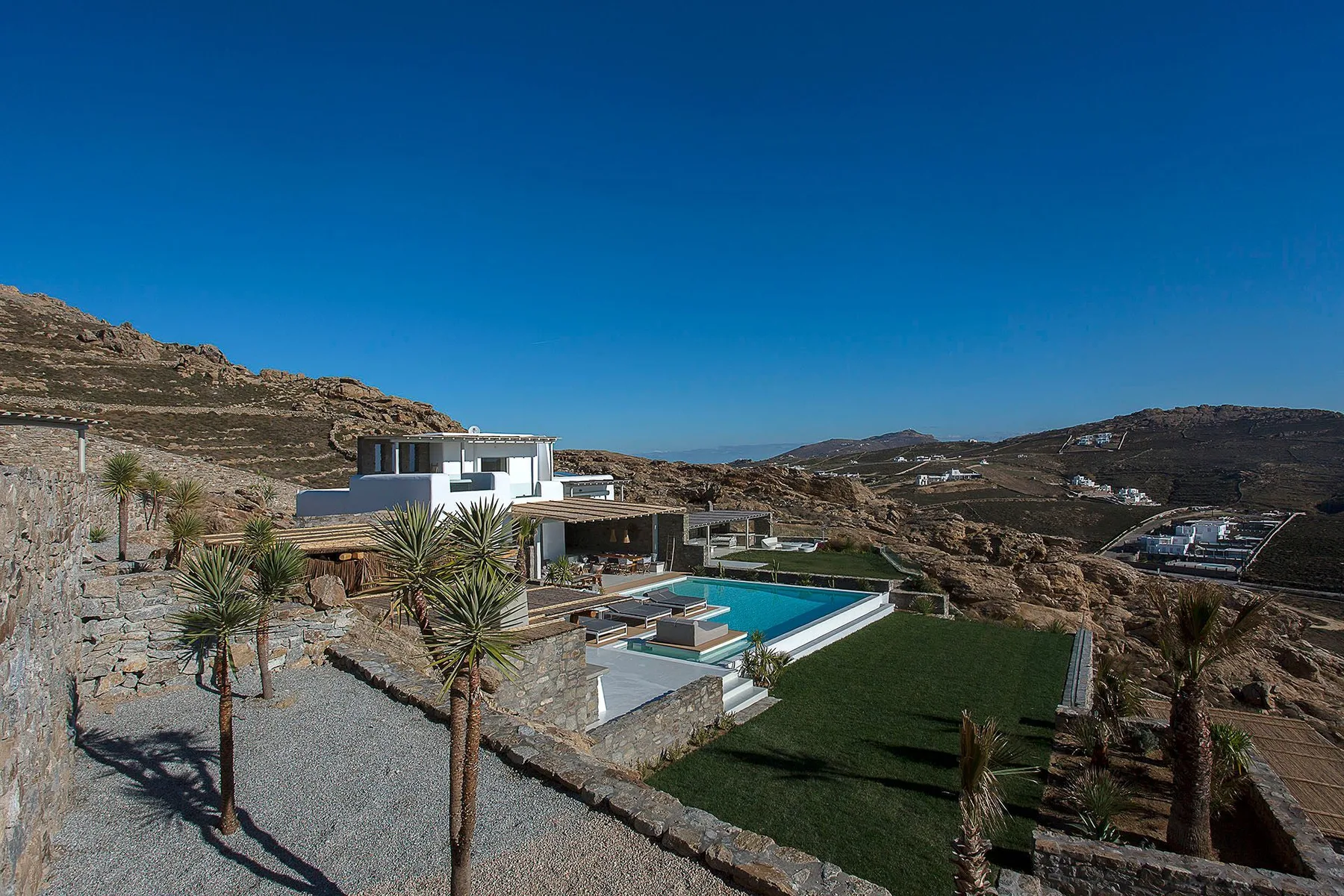 A modern house and swimming pool sit among dry, rocky hills.