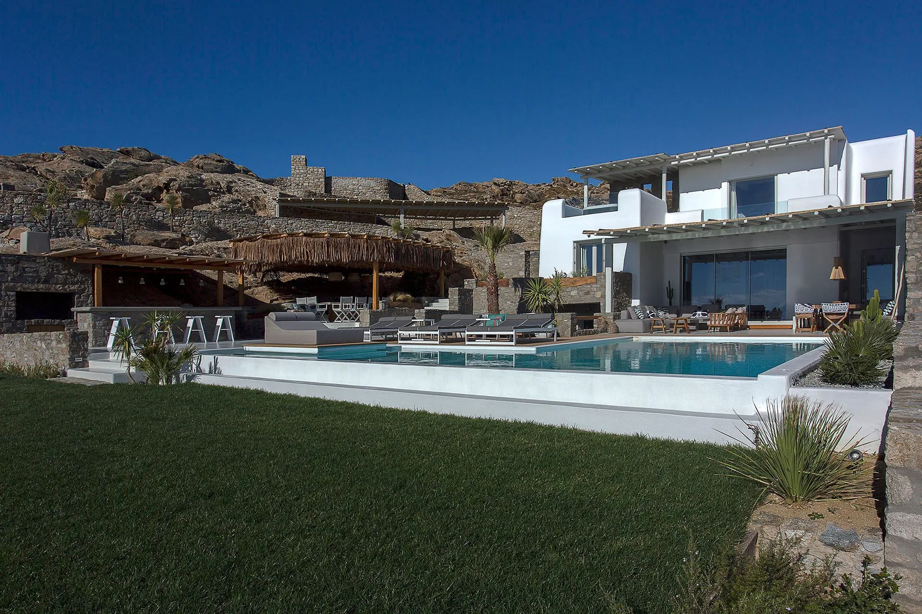 A modern white house overlooks a swimming pool and green lawn.
