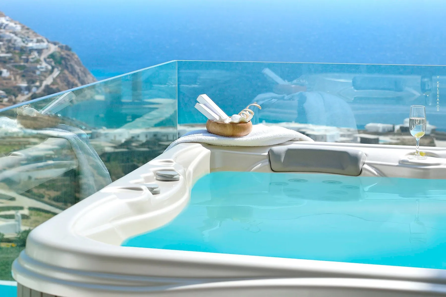 A rooftop hot tub overlooks the sea through a glass railing.