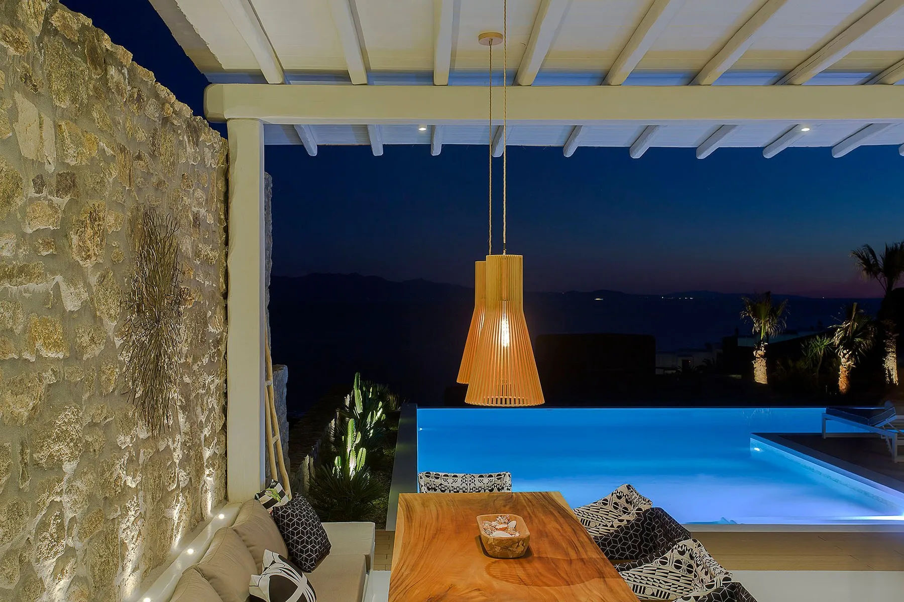 An outdoor seating area overlooks a glowing pool beneath a covered terrace.