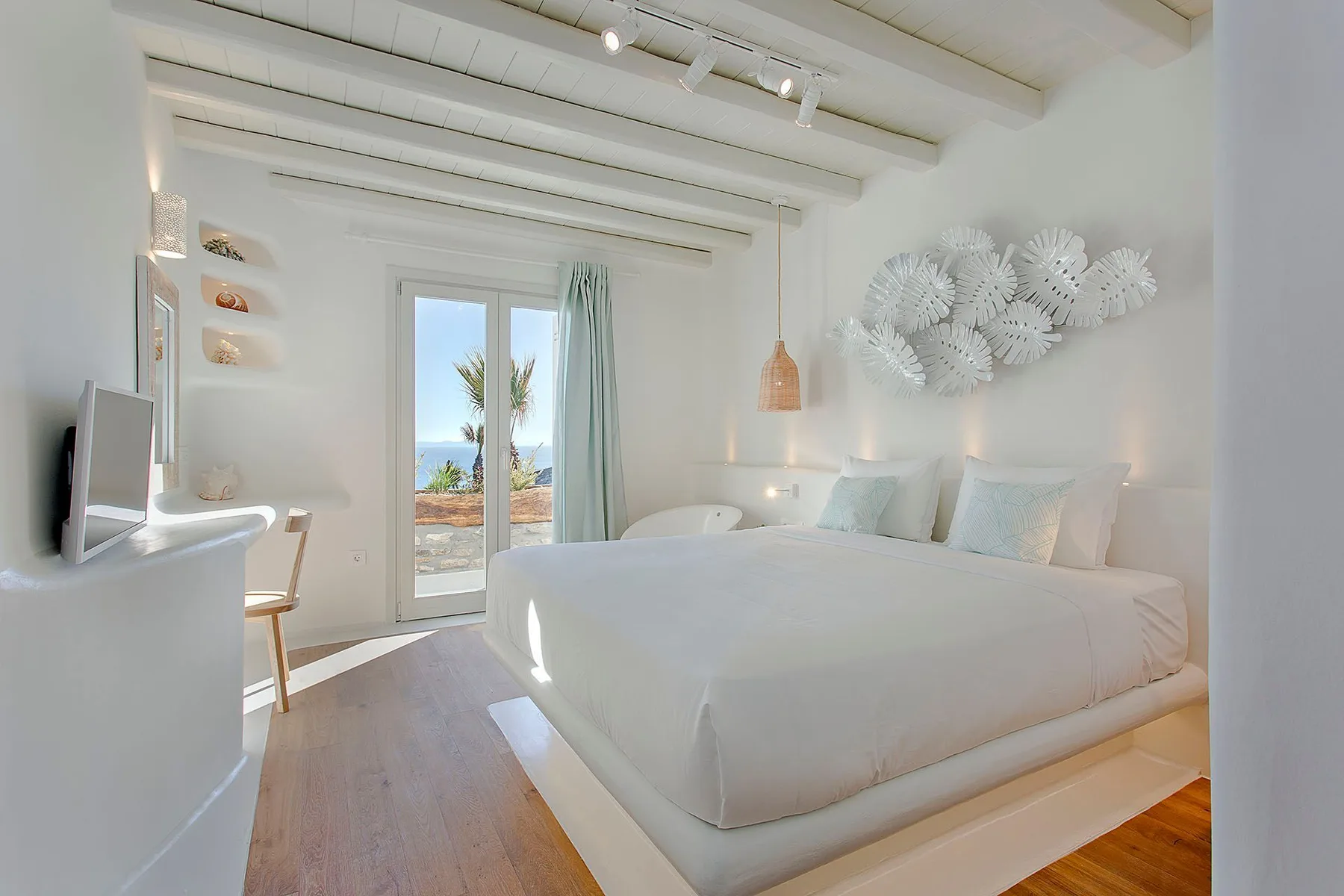 A bright bedroom with a large bed and glass doors opening to a balcony.