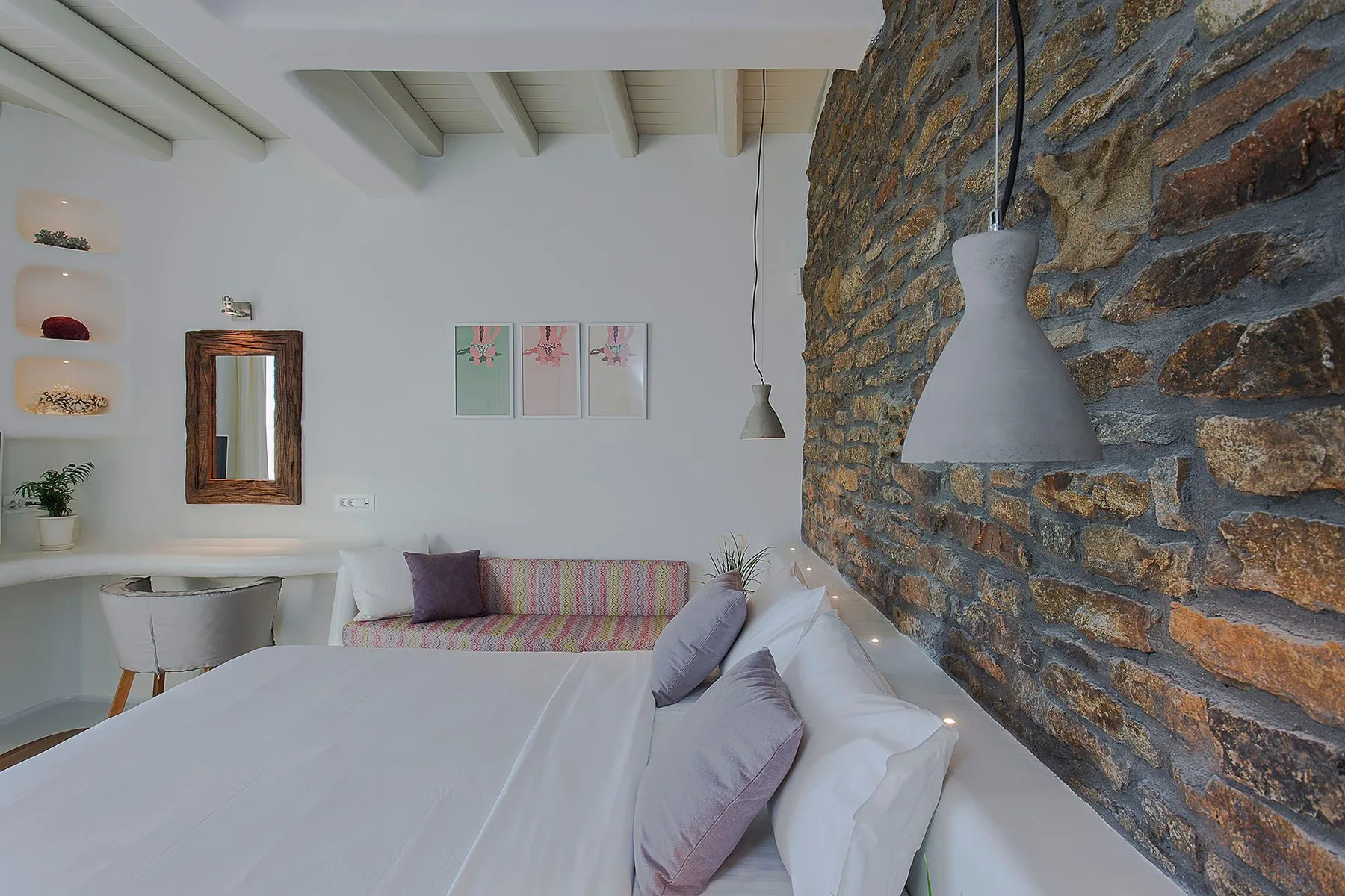 A bedroom with a neatly made bed beside a rustic stone wall.