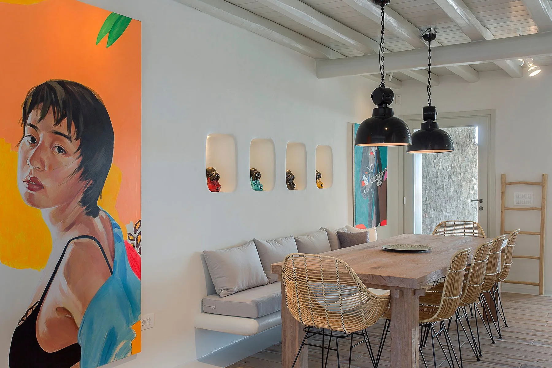 A dining area with a long table, woven chairs, and colorful wall art.