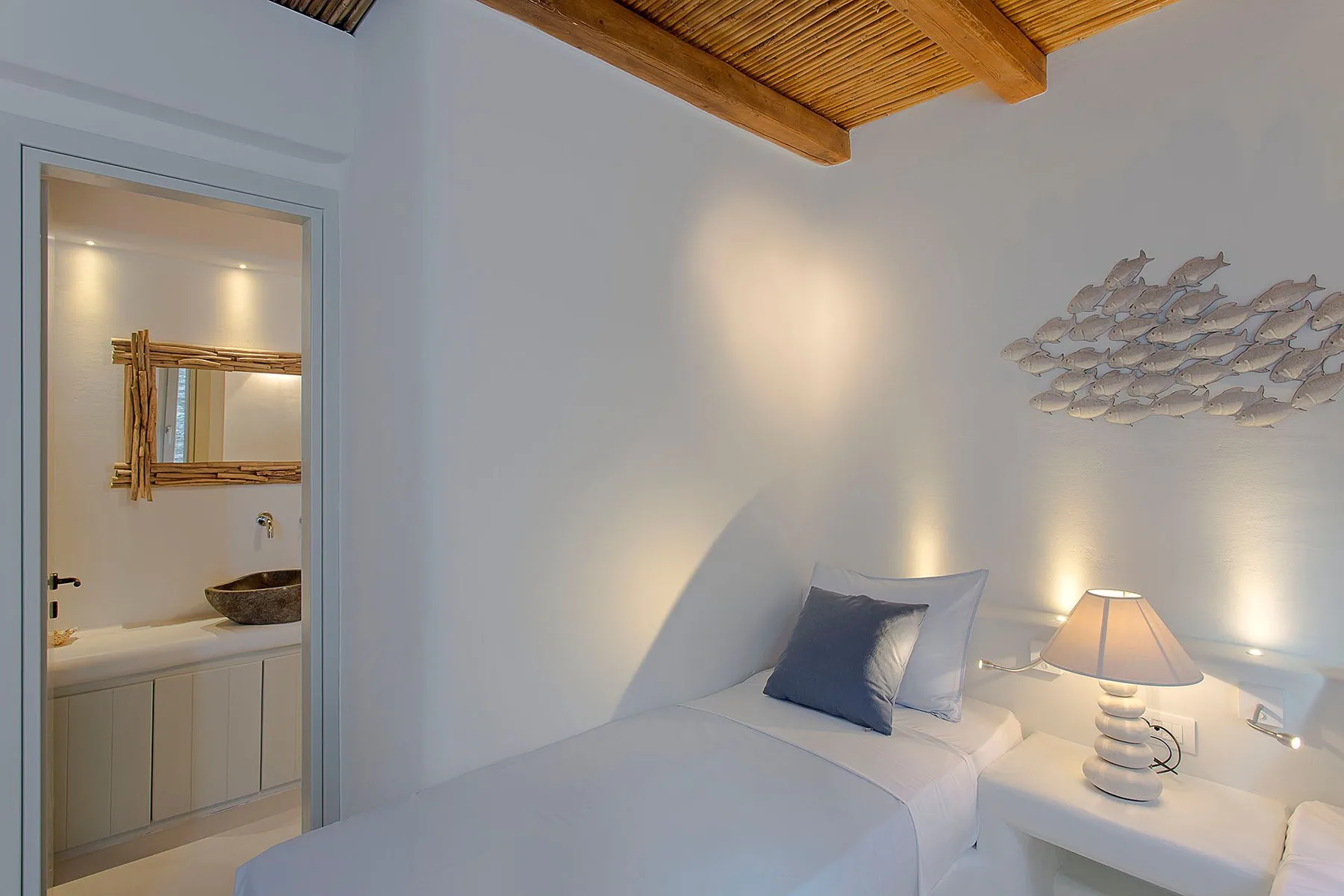 A bedroom with a neatly made bed, bedside lamp, and woven ceiling.