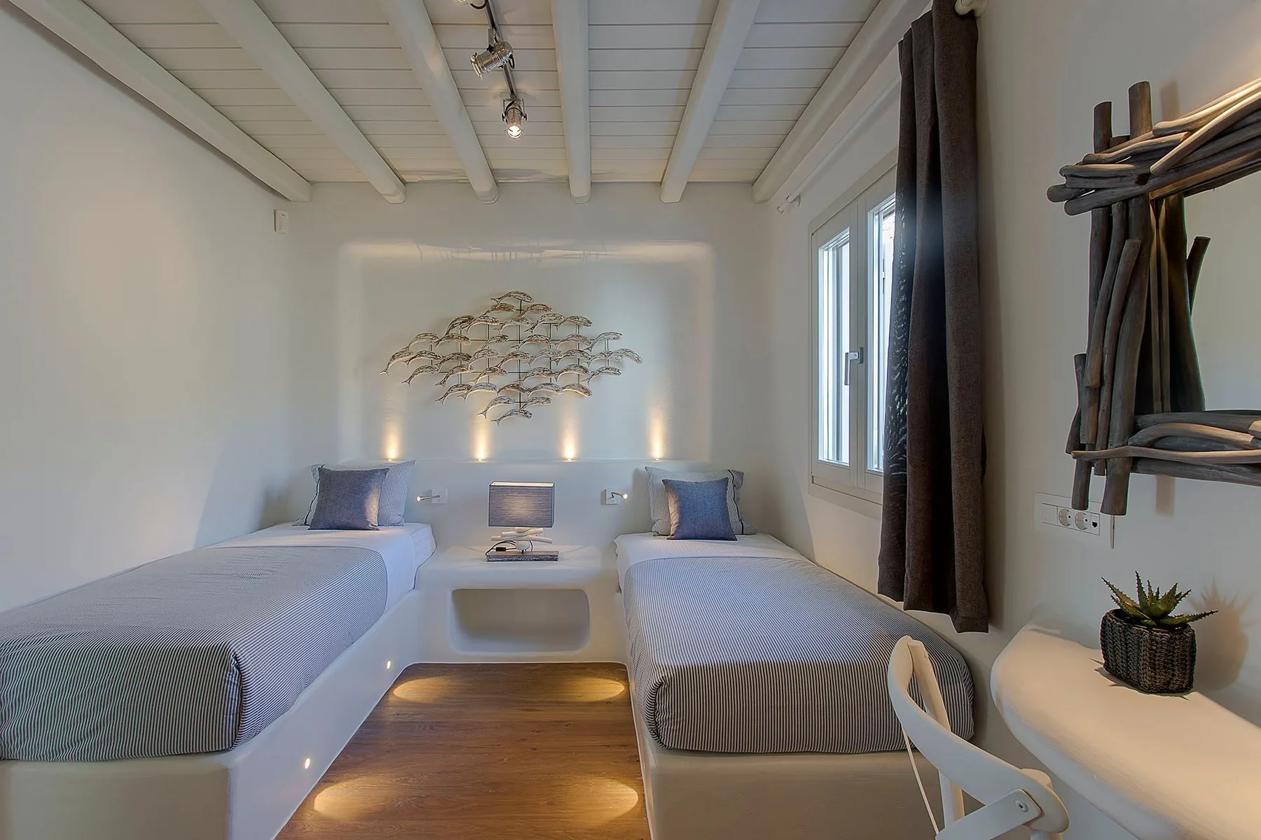A bright bedroom with two single beds, a small table, and wall art.