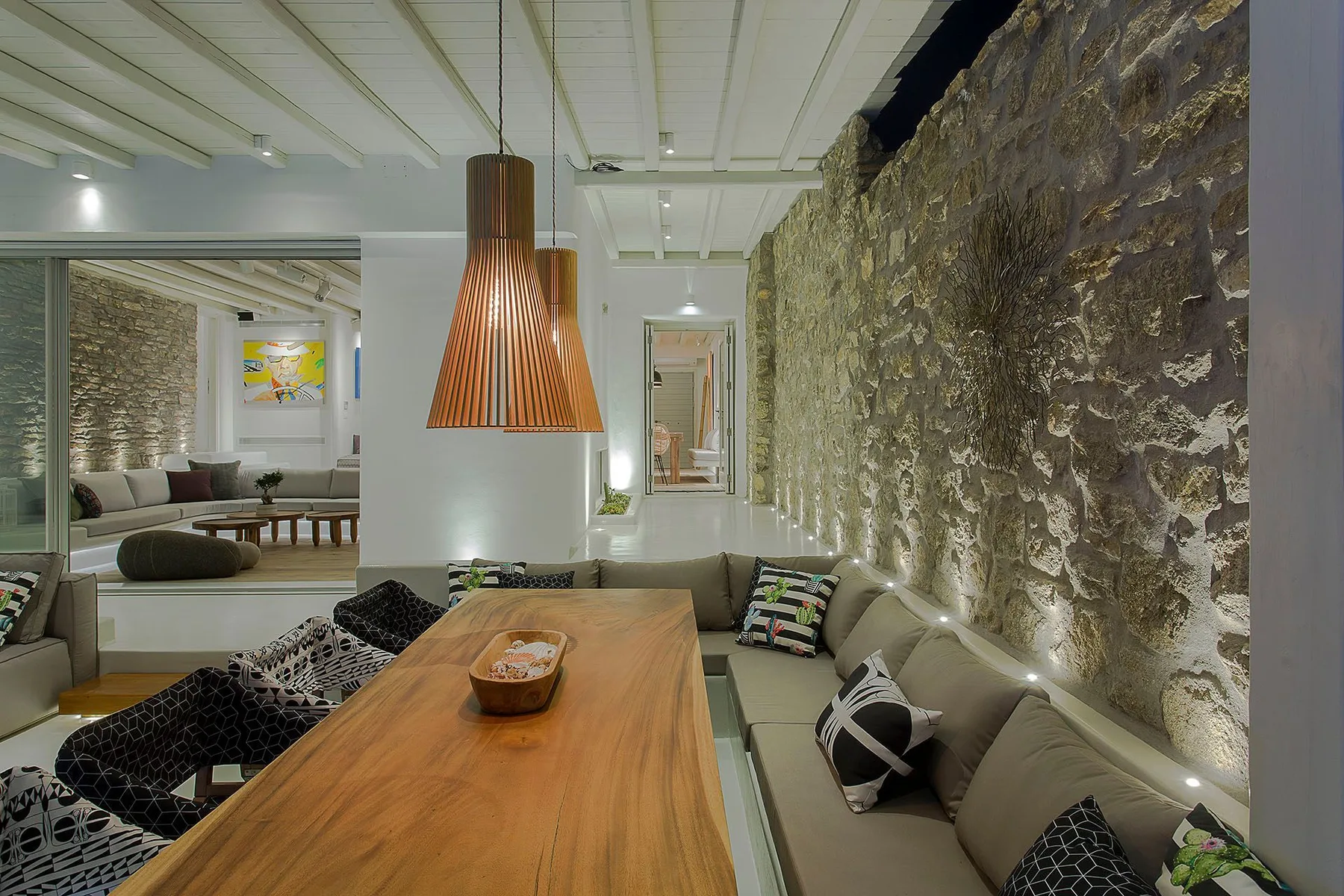 A dining area with a long wooden table, built-in seating, and an exposed stone wall.