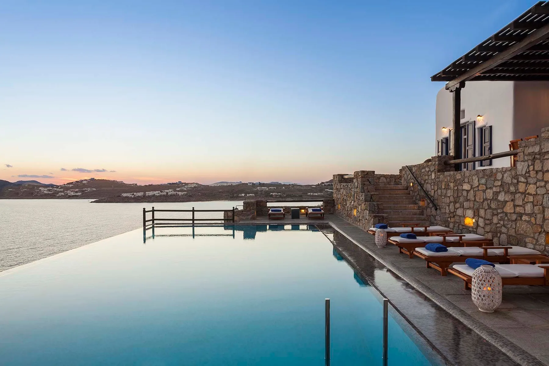 An outdoor pool beside a stone terrace overlooks the water at dusk.