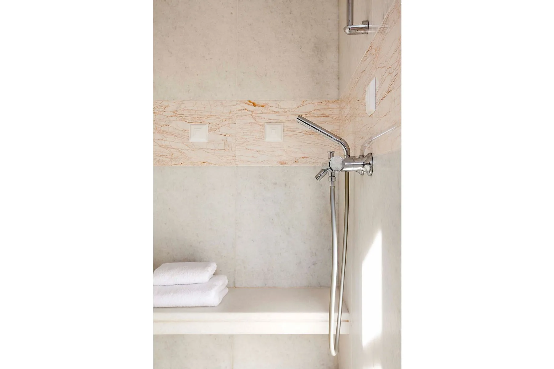 A tiled shower area with a handheld showerhead and folded towels on a ledge.