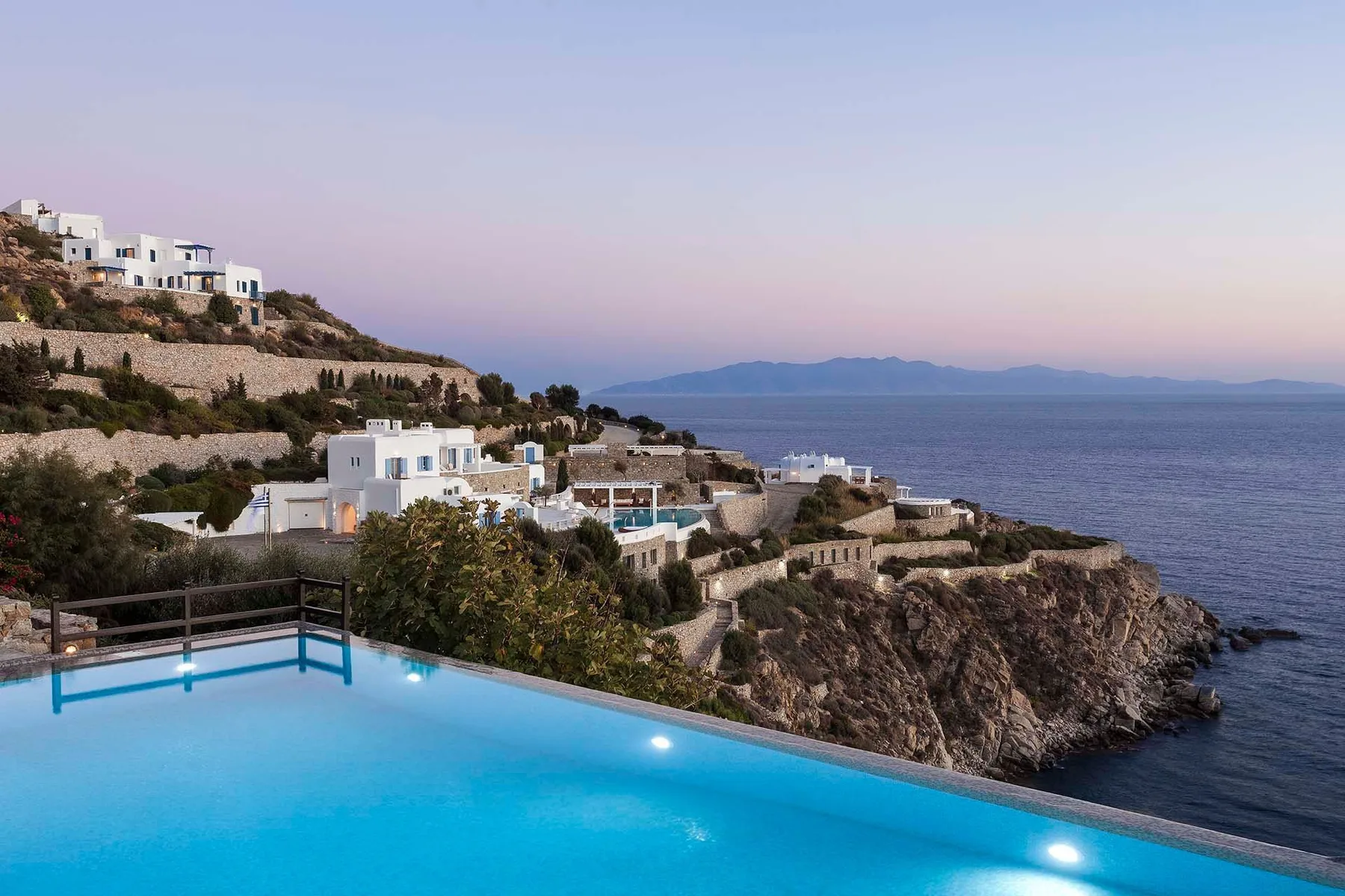A hillside coastal scene with white buildings, a swimming pool, and the sea.