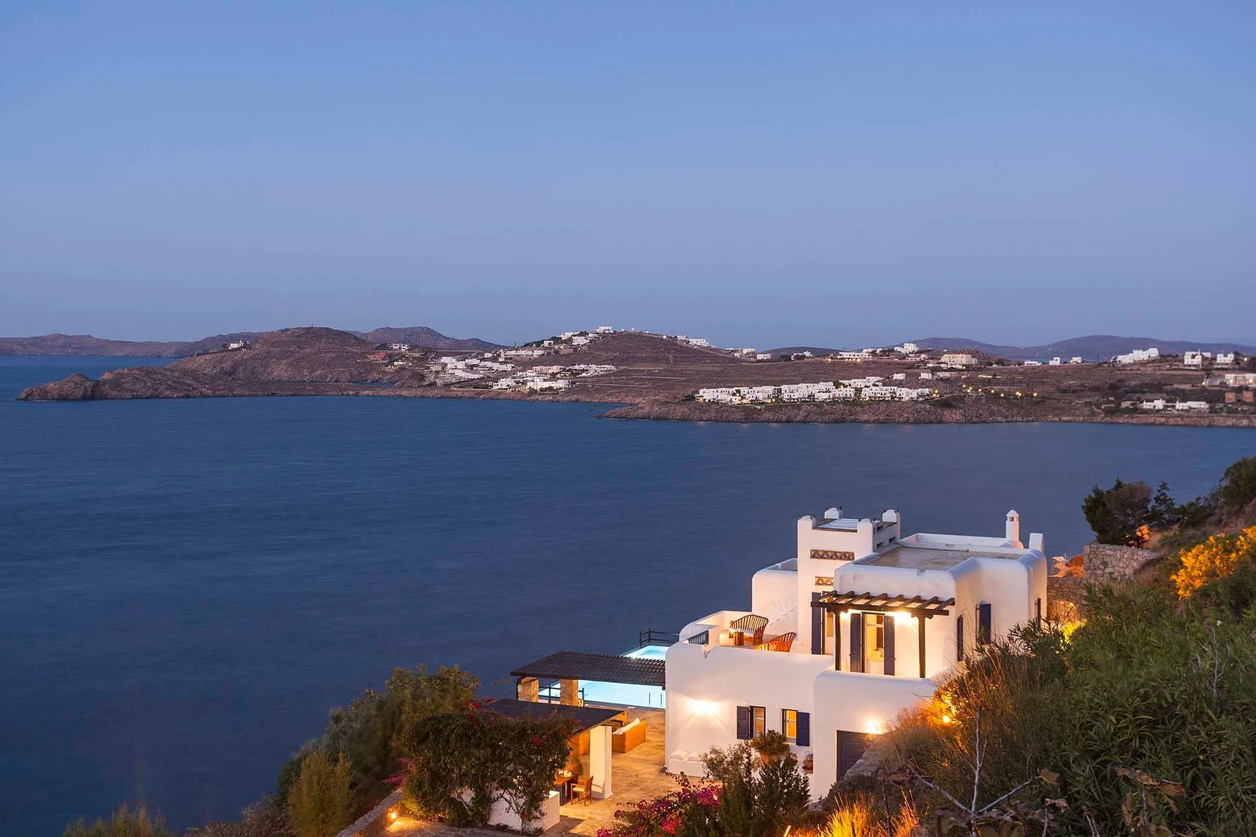 A coastal scene shows a white building above the water, with distant hills across the bay.