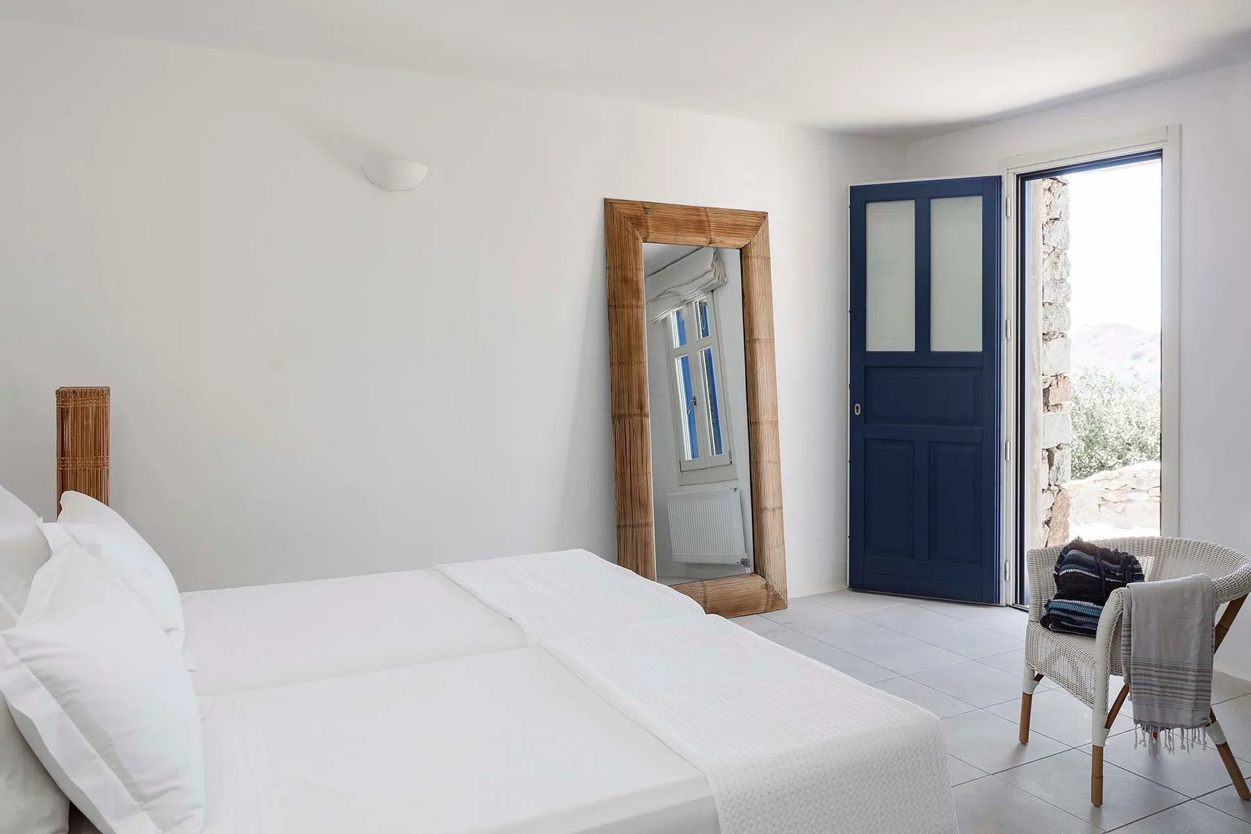 A bright bedroom with white bedding, a mirror, and an open blue door.