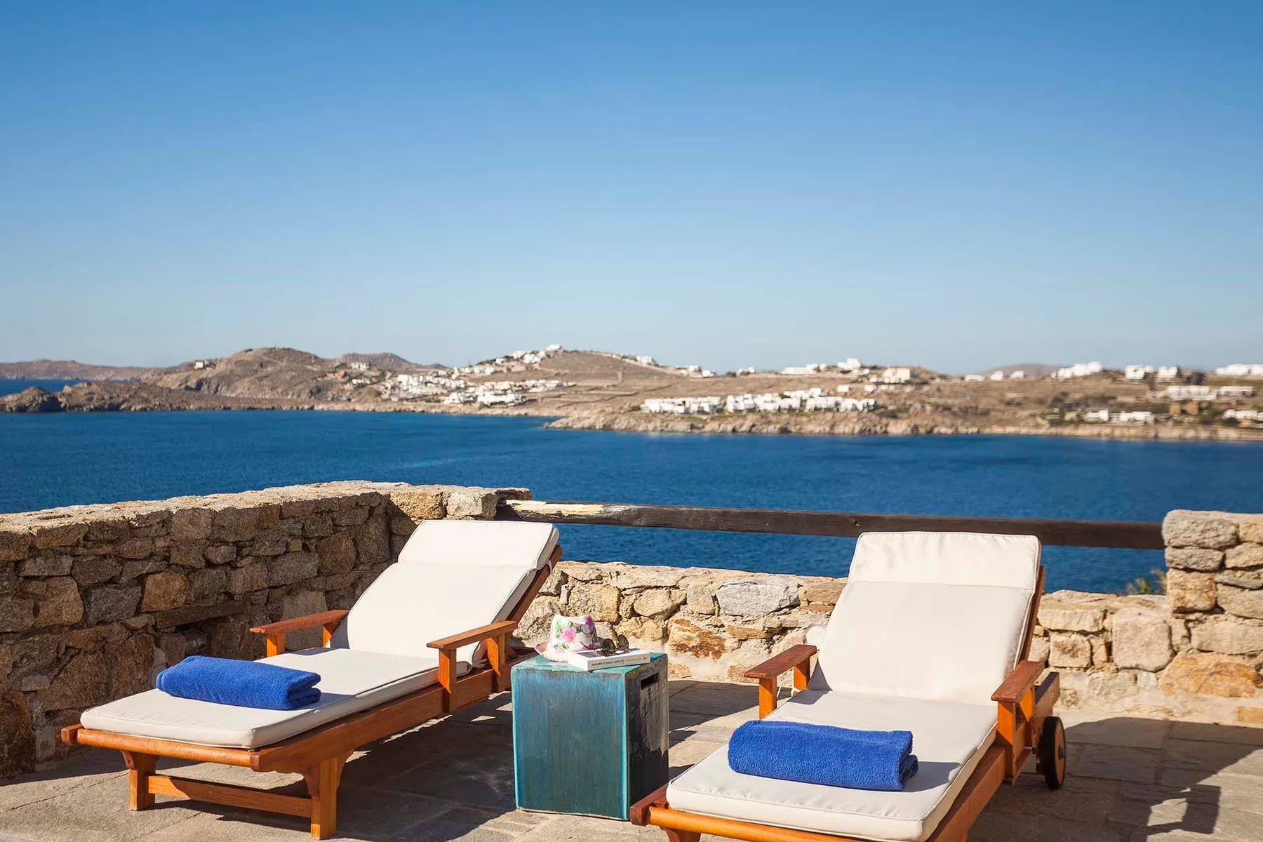 A sun terrace overlooks the sea, with lounge seating beside a low stone wall.