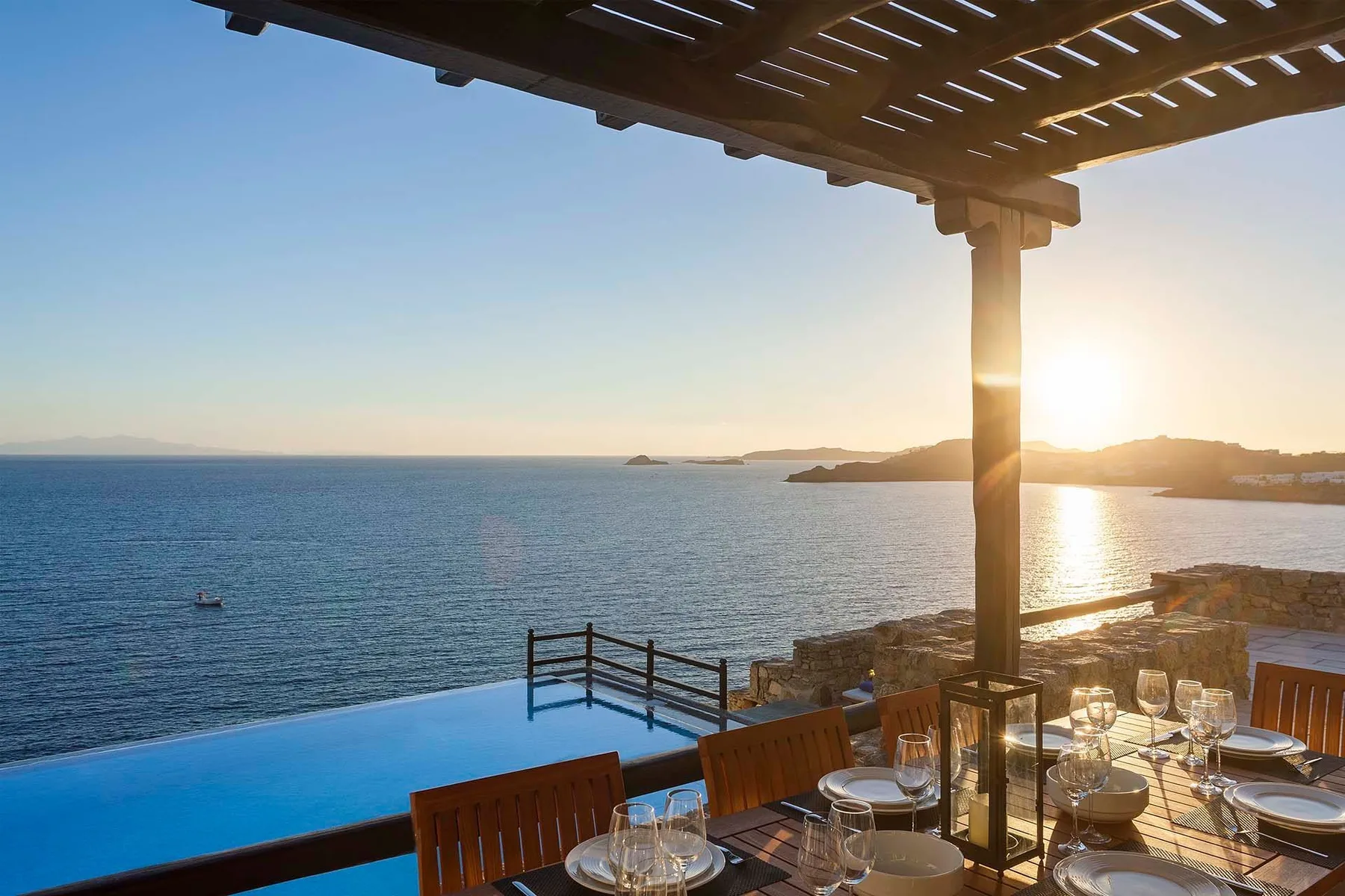 A seaside dining terrace overlooks the water at sunset, with a pool beside it.