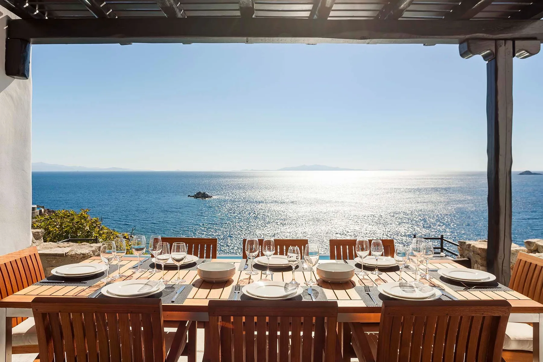 An outdoor dining table faces the sea beneath a shaded pergola.