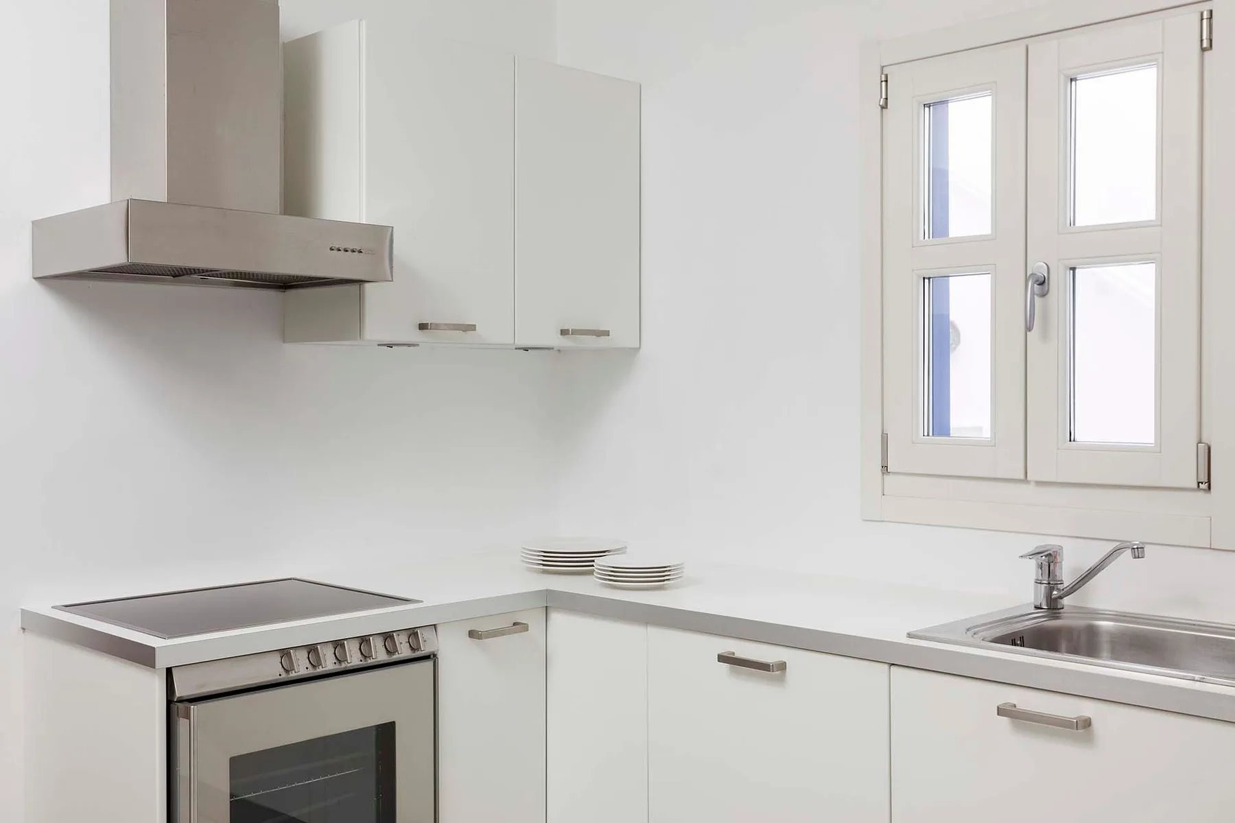 A bright white kitchen with a stovetop and sink beneath a window.