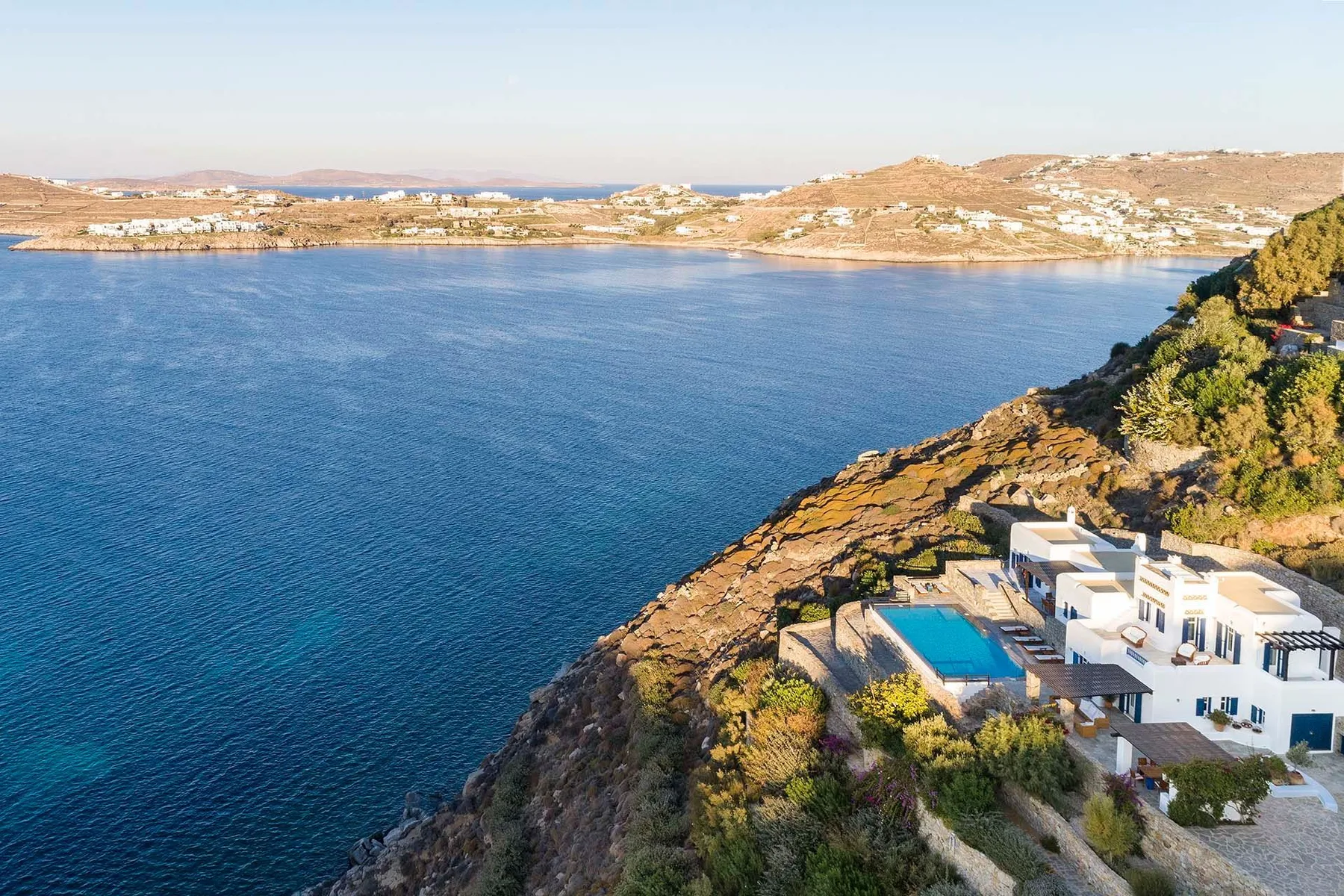 A coastal resort sits beside a broad blue bay, with a swimming pool near the shore.