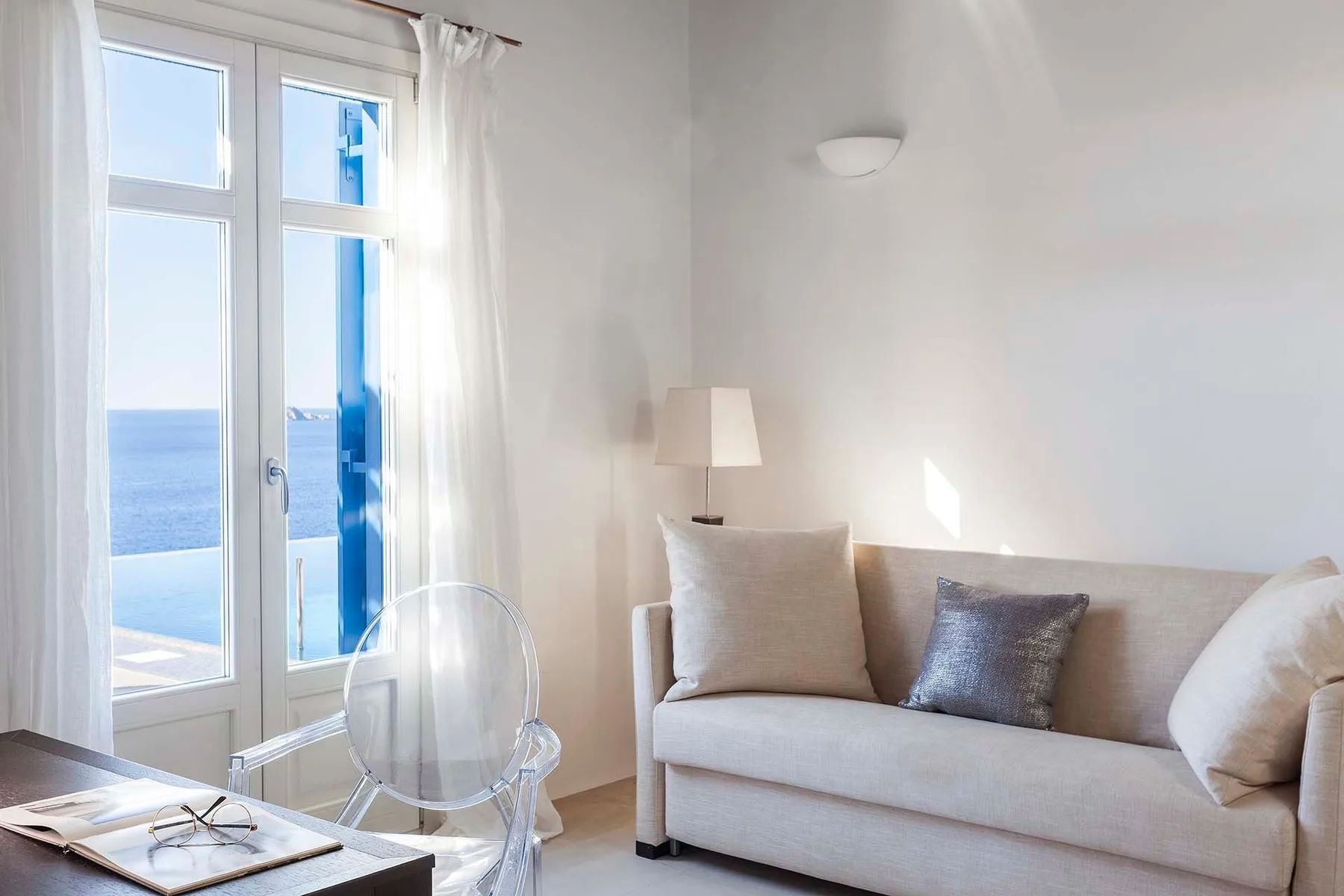 A bright living room with a sofa beside tall windows overlooking the sea.