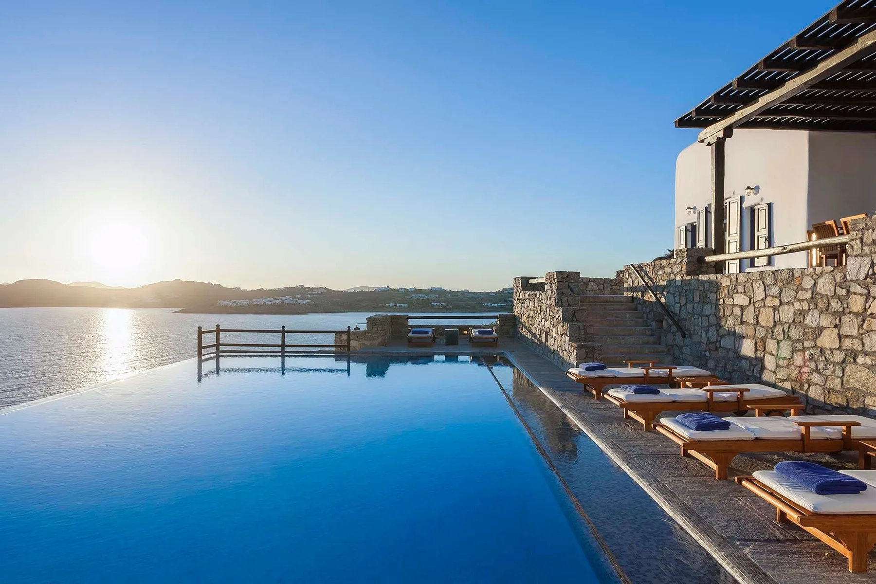 An outdoor pool overlooks the water, with lounge seating along the stone terrace.