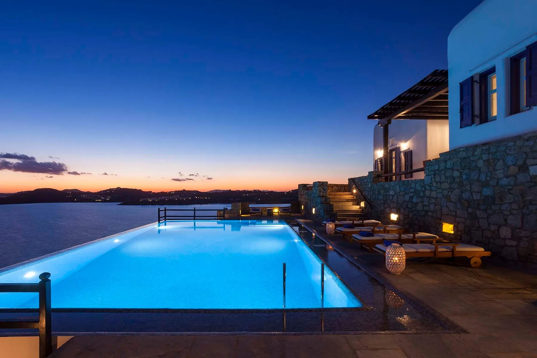 An illuminated swimming pool beside outdoor seating at sunset.
