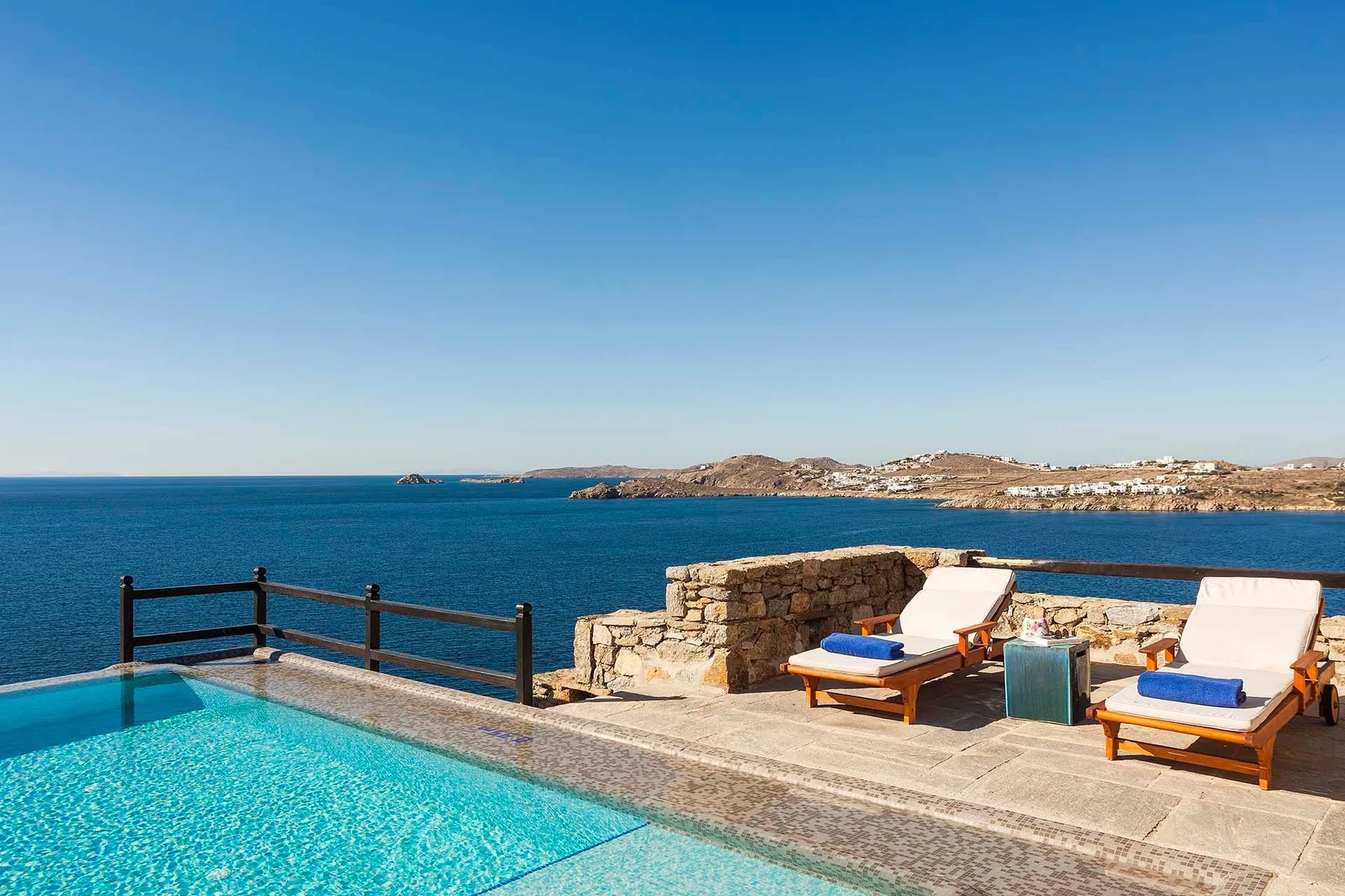 A poolside terrace overlooks the sea, with sun loungers beside the water.